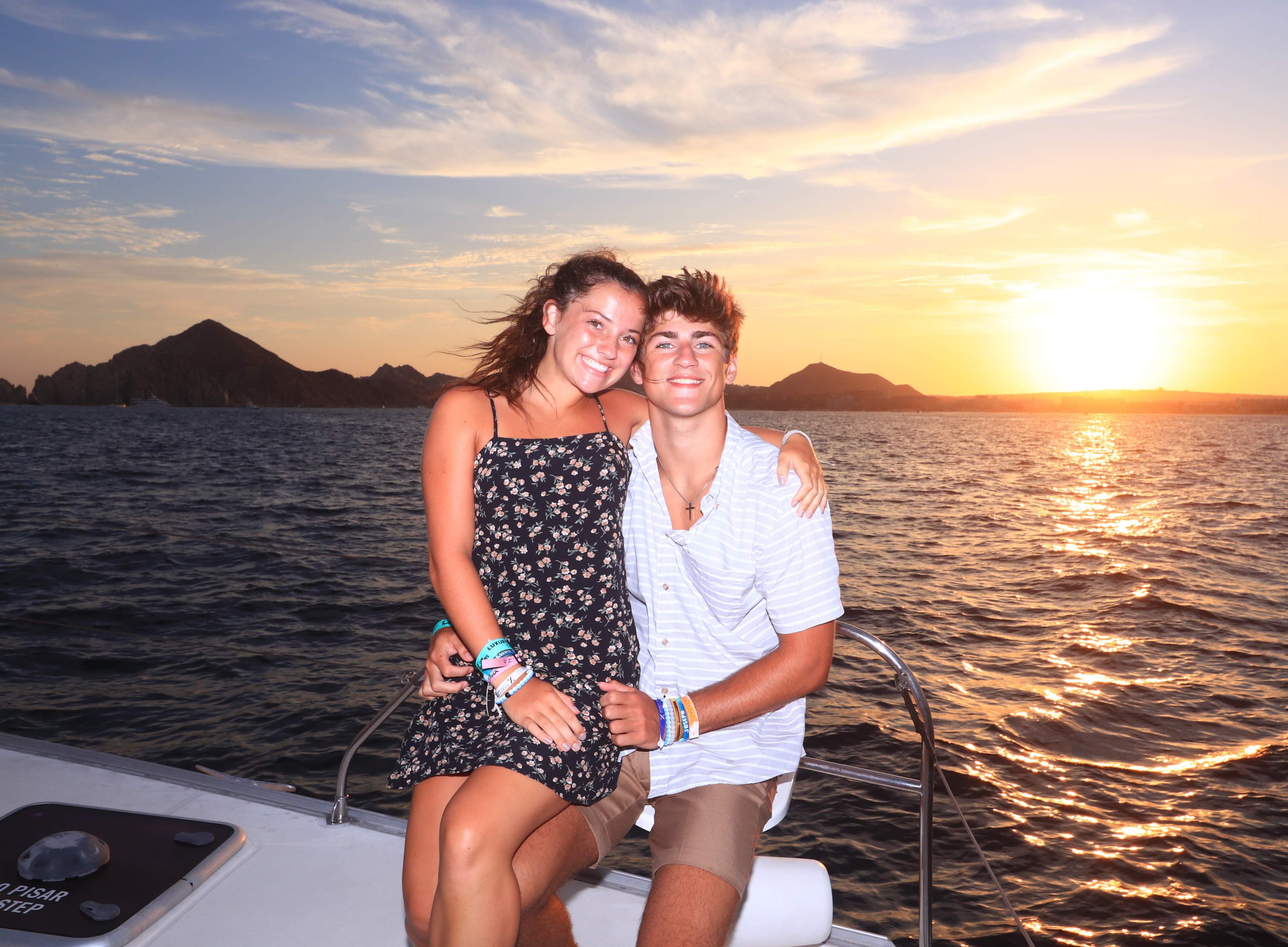 Couple embracing on a Cabo Adventures catamaran at sunset in Cabo, with golden light reflecting on the ocean.