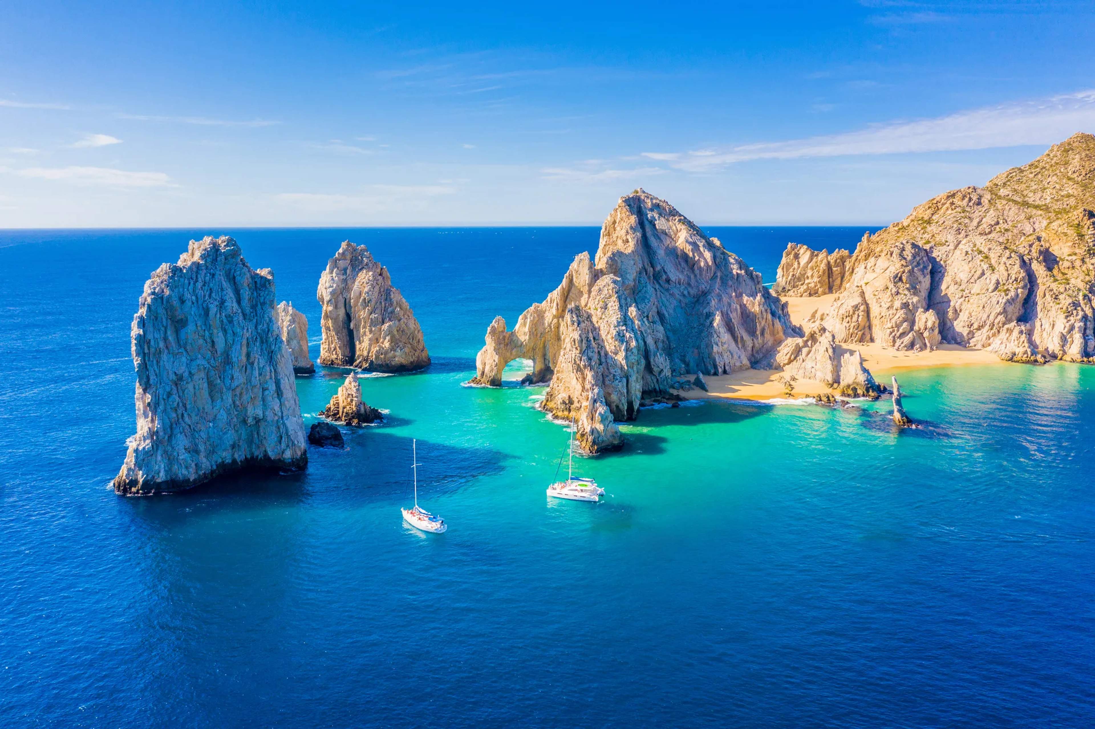 Aerial view of El Arco and surrounding rock formations with sailboats anchored in turquoise waters near Cabo San Lucas.