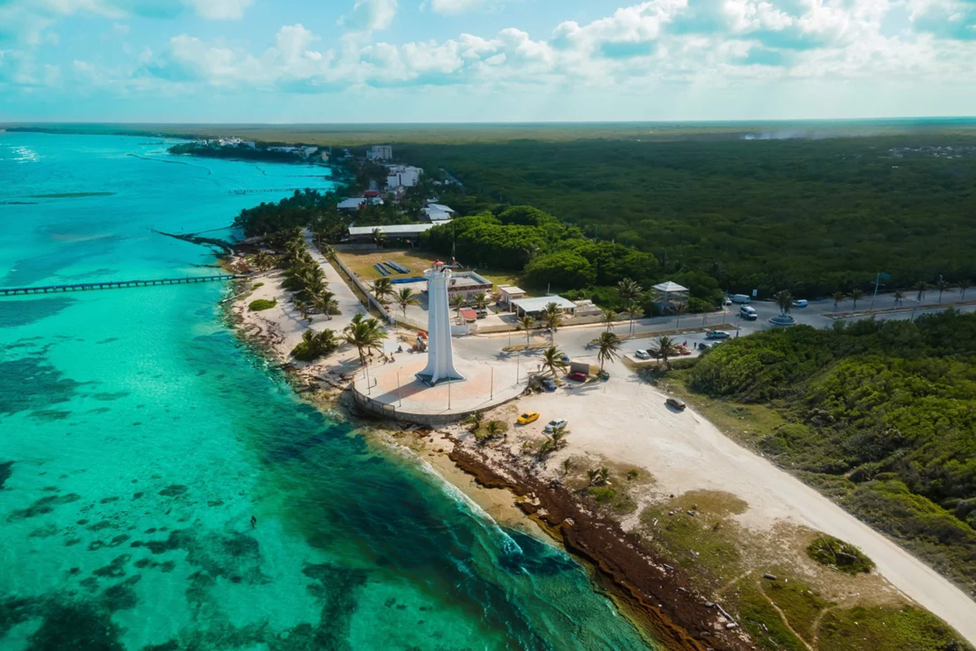 A white lighthouse stands by turquoise waters and palm trees on the peaceful coast of Mahahual.