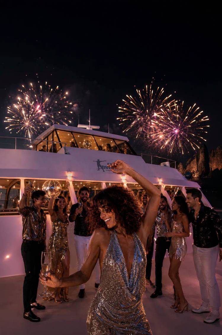Guests dance and celebrate New Year’s Eve Disco Fever aboard Oceanus by Cabo Adventures as fireworks light up Cabo's Bay.