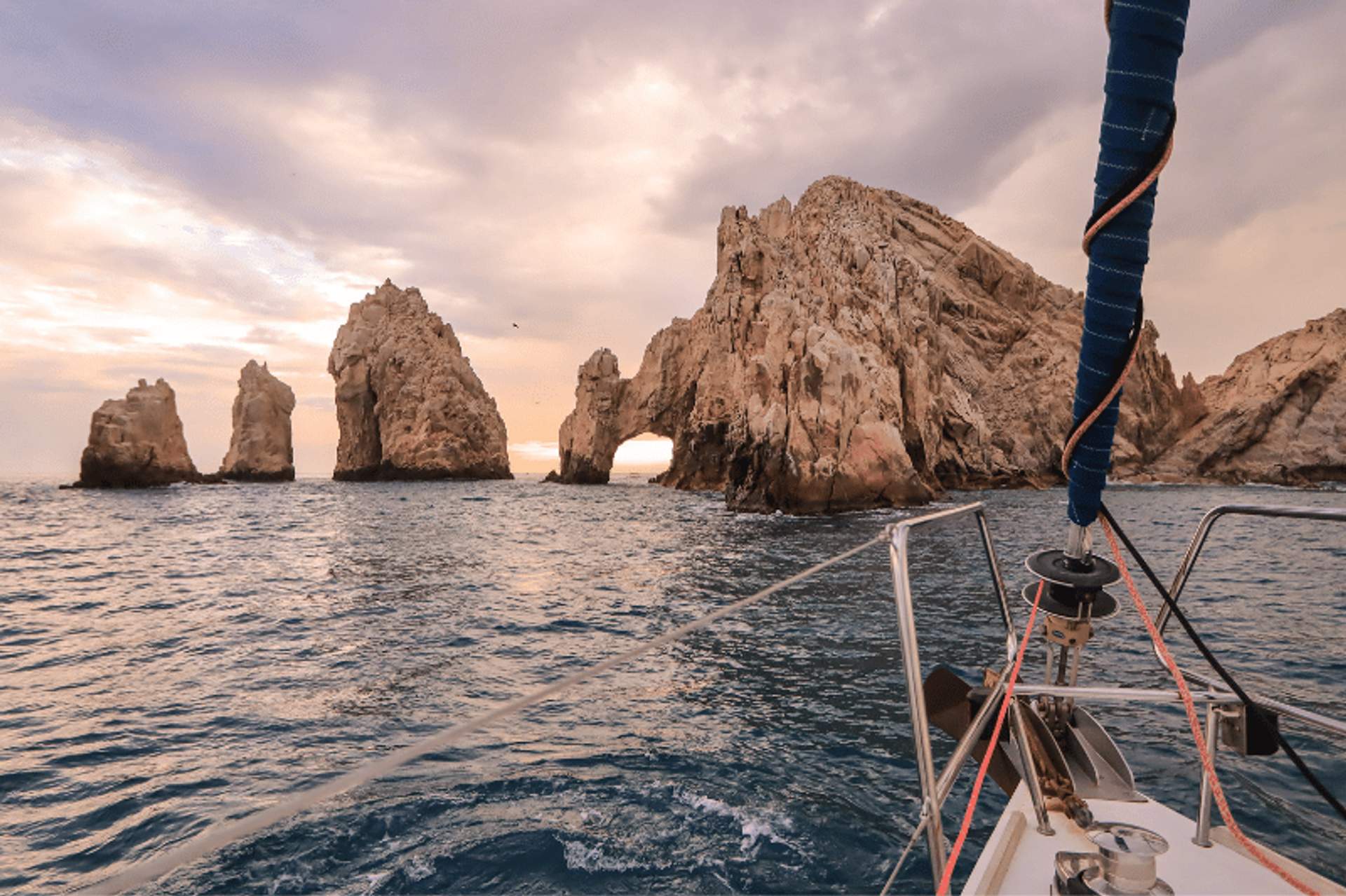 Vista de la formación rocosa El Arco en el Fin de la Tierra en Cabo San Lucas desde la proa de un velero al atardecer.