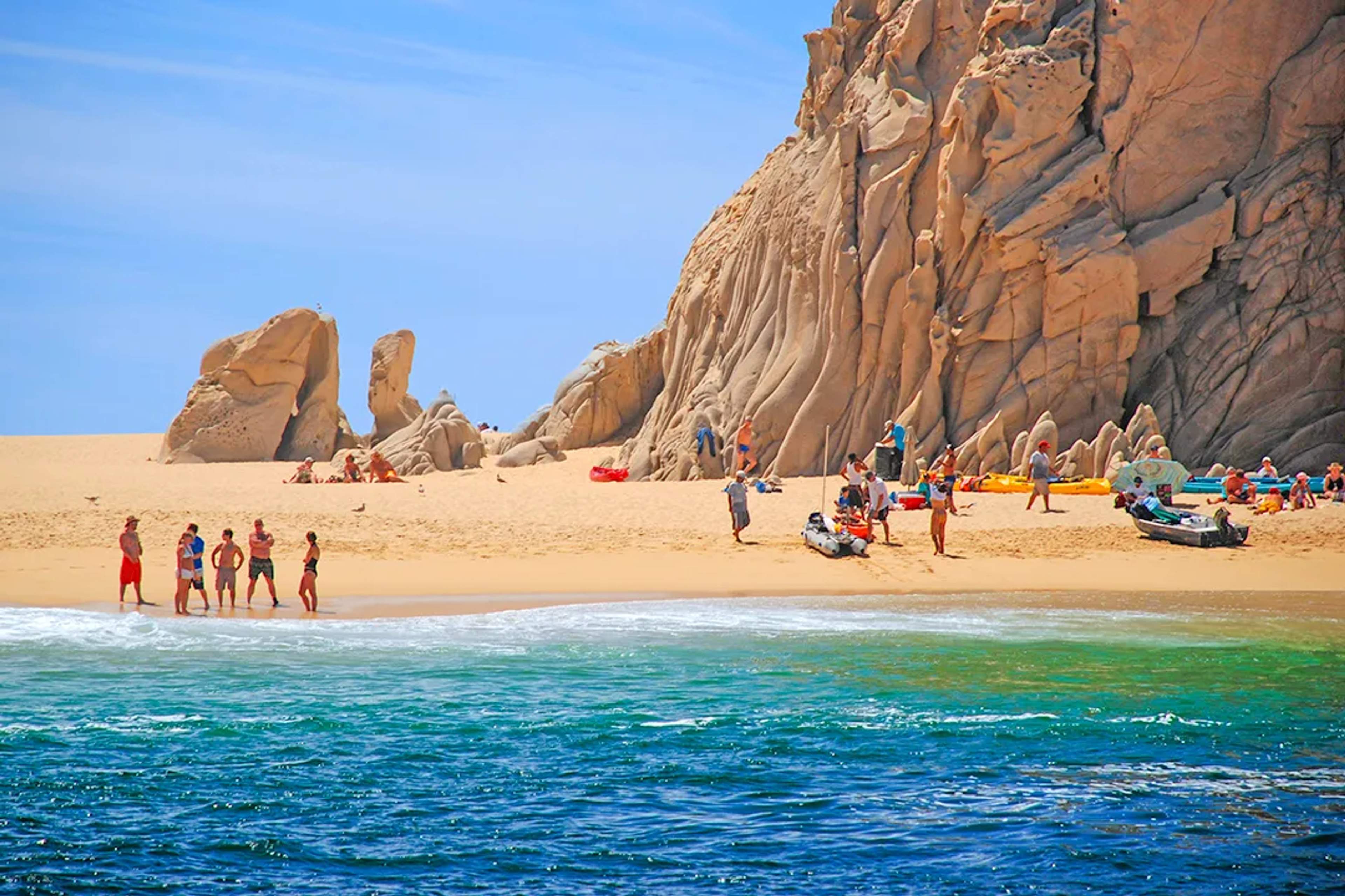 Visitantes disfrutando una playa aislada en Cabo San Lucas, con arena dorada, agua turquesa y formaciones rocosas increíbles