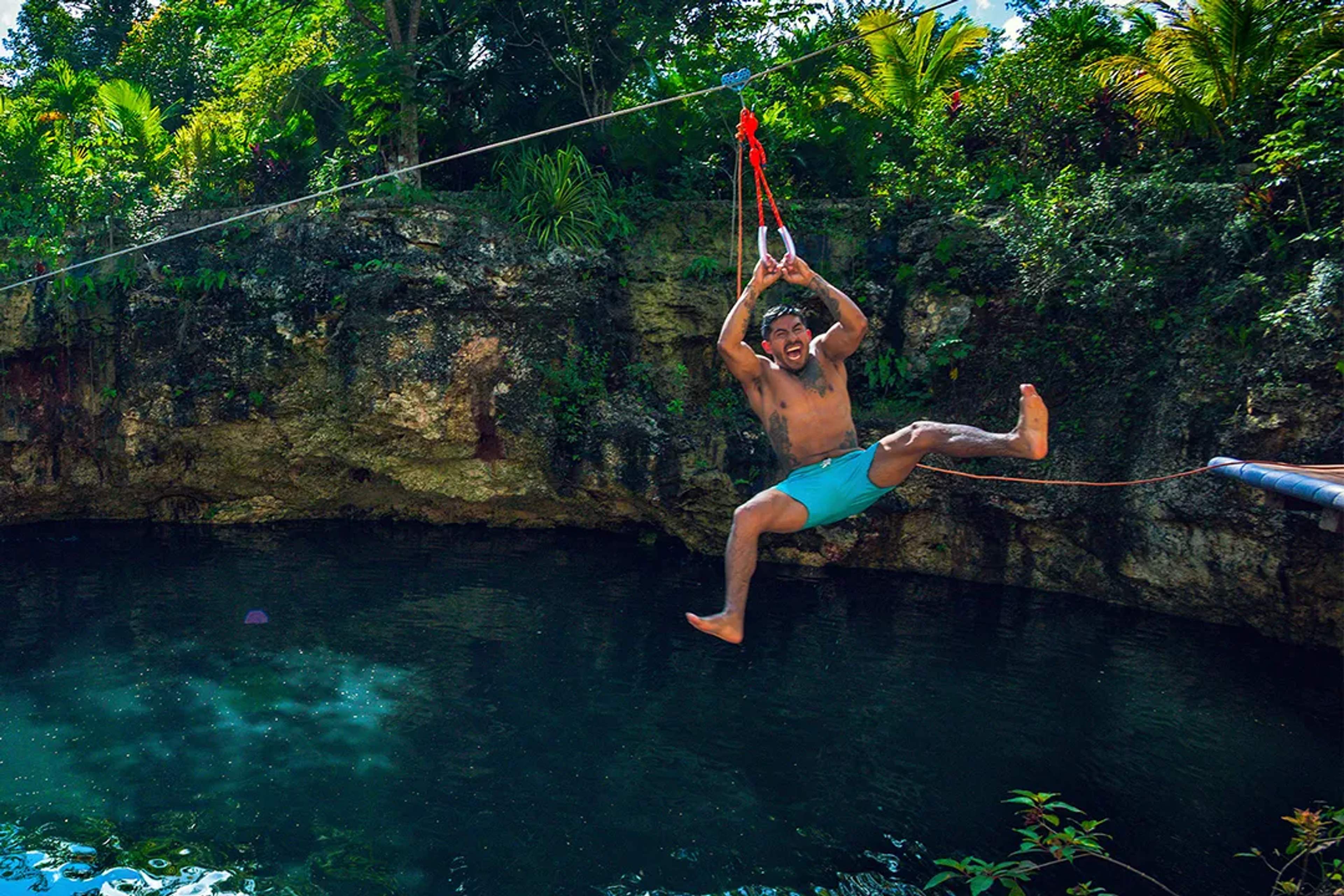 Guest zip-lining over a natural jungle cenote, splashing into crystal-clear water on an adventure tour in Puerto Vallarta