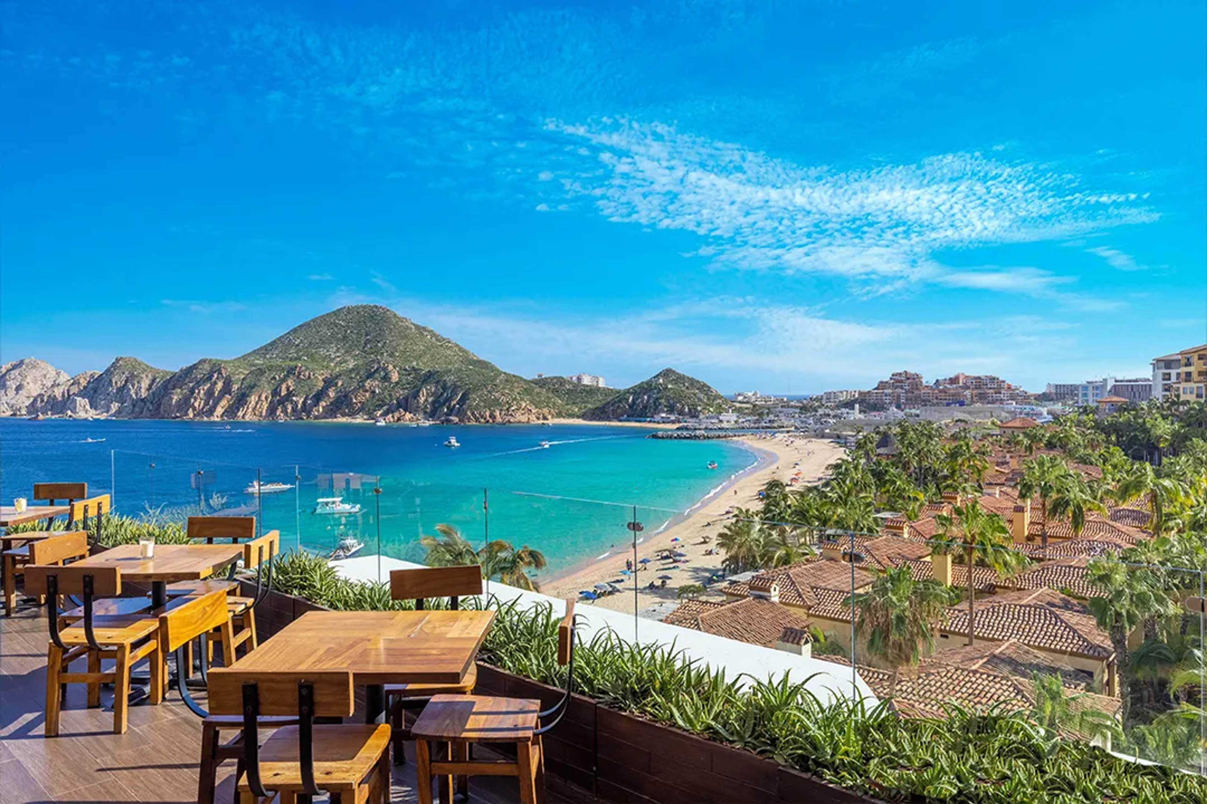 Vista panorámica de Playa El Médano y la bahía desde un restaurante con mesas y cielo azul.