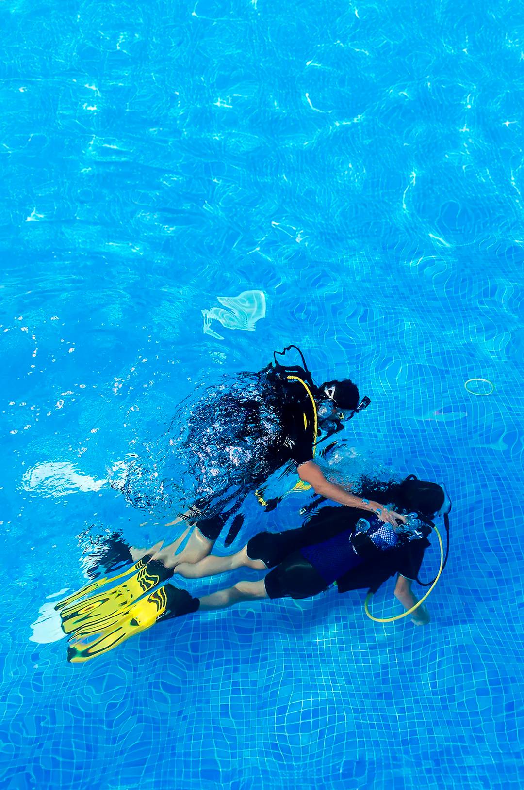 Instructor de buceo asiste a un alumno bajo el agua durante práctica con aletas llamativas.