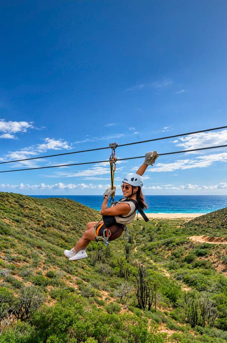 Woman ziplining over desert hills with ocean views on Pacific Zipline Adventure by Cabo Adventures.