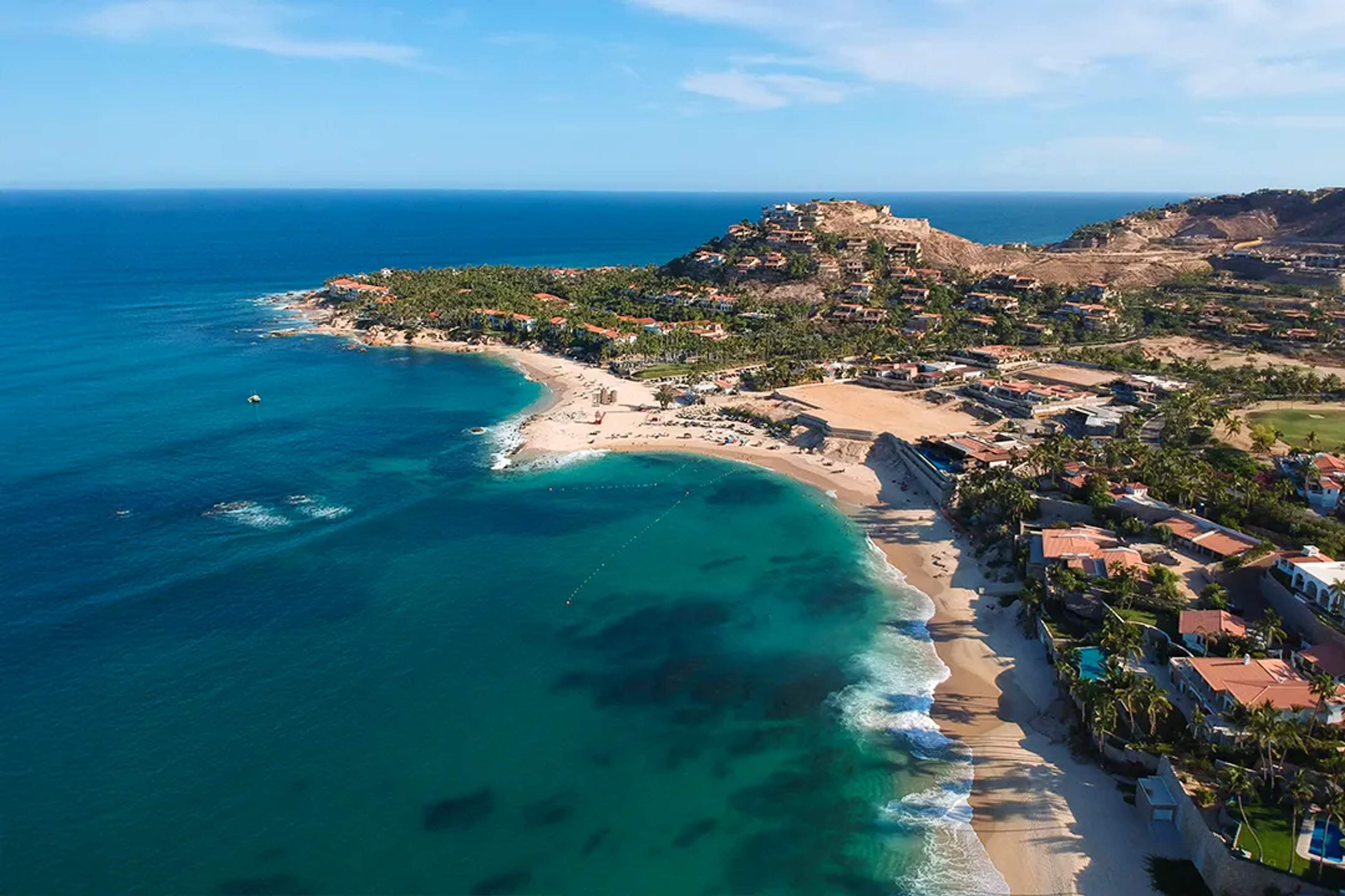 Una playa serena con arena dorada, aguas turquesas y rocas dispersas, ideal para una escapada tranquila bajo el sol.