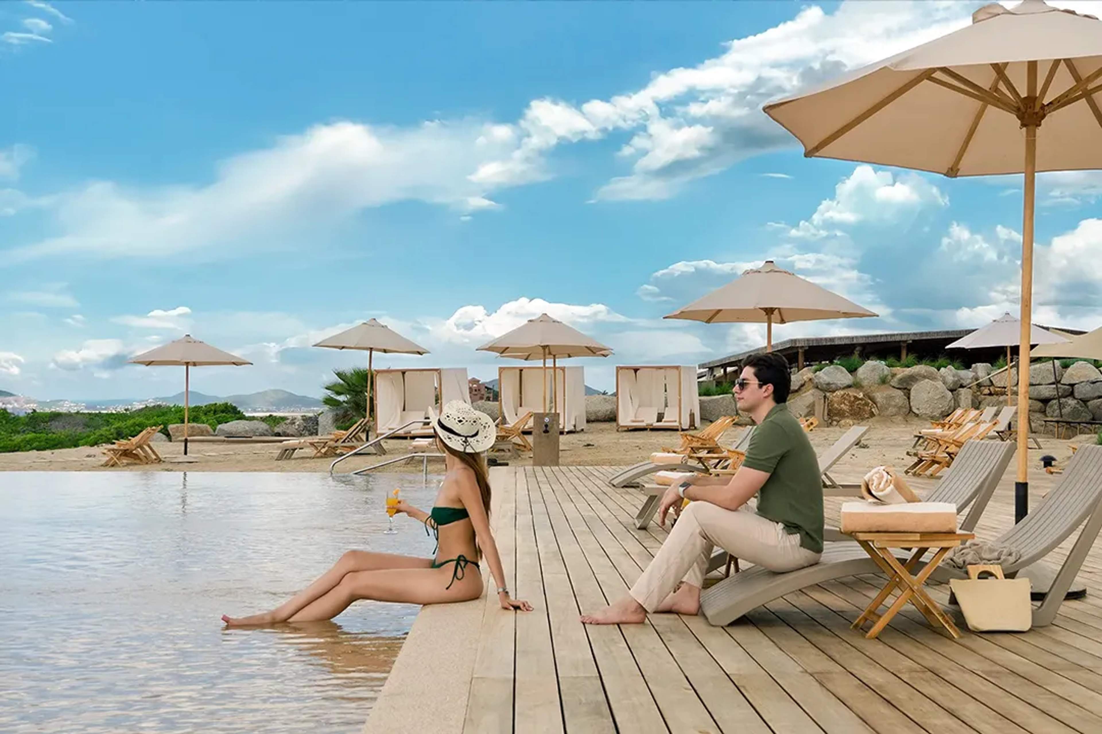 Pareja relajándose en una alberca infinita frente al mar con camastros y sombrillas en Los Cabos.
