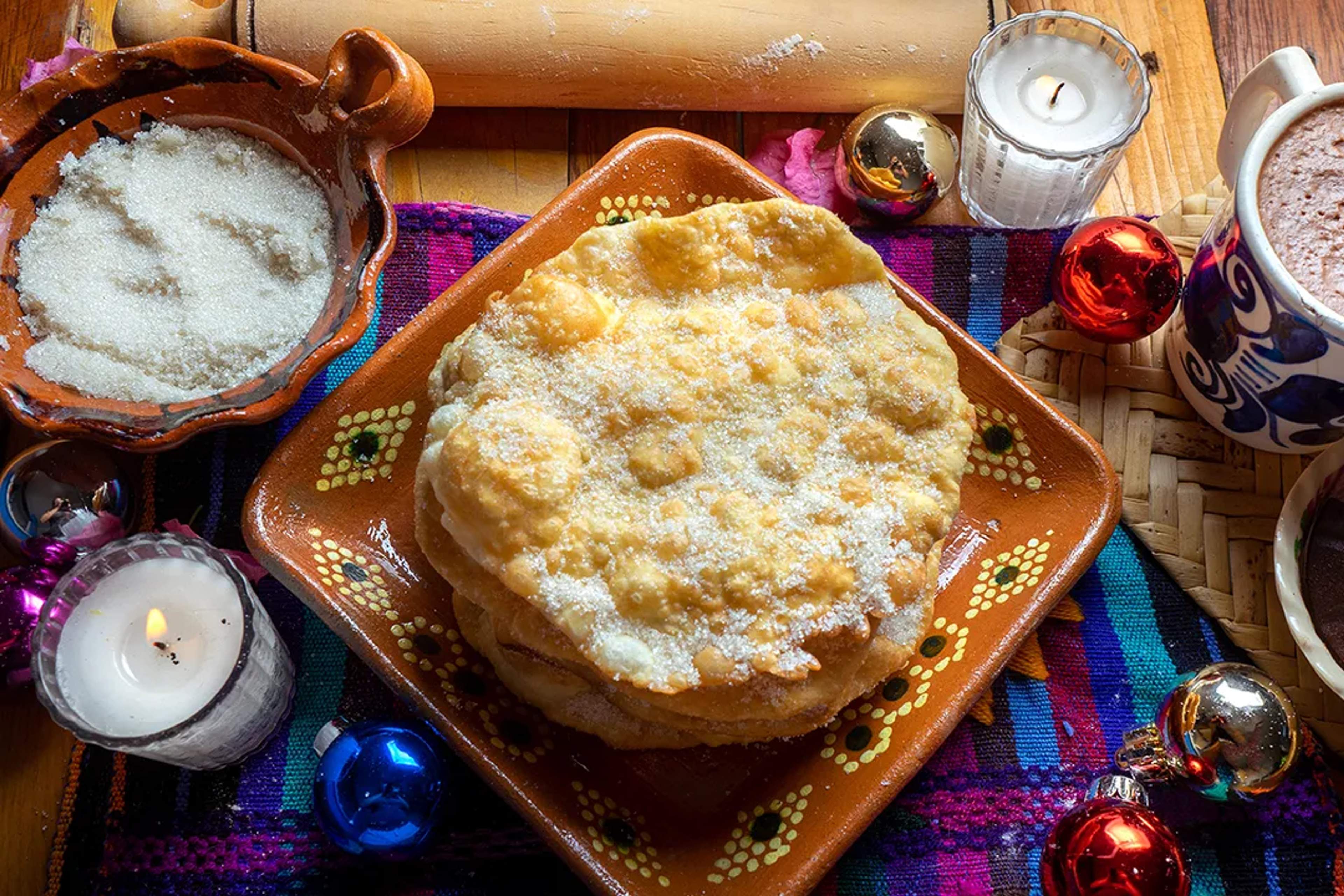 Traditional Mexican buñuelos dusted with sugar, served with hot chocolate and festive decor.