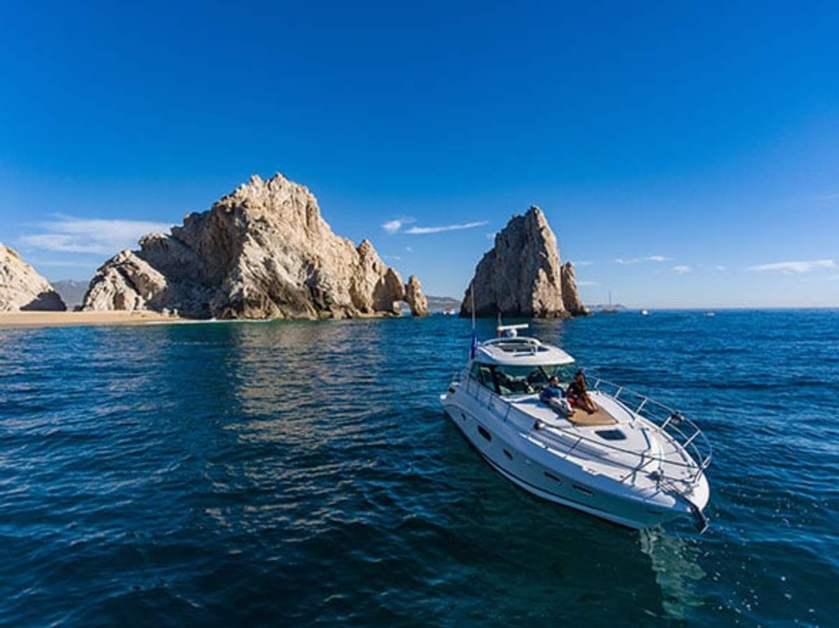 A luxury yacht floats on calm blue waters near striking rock formations under a clear sky. The serene setting suggests a leisurely day at sea with scenic coastal views.