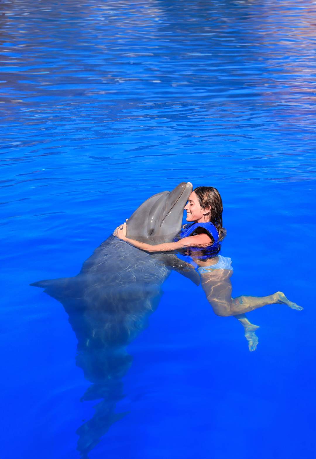 Woman lovingly hugs a dolphin in the water, sharing a heartfelt moment of connection.