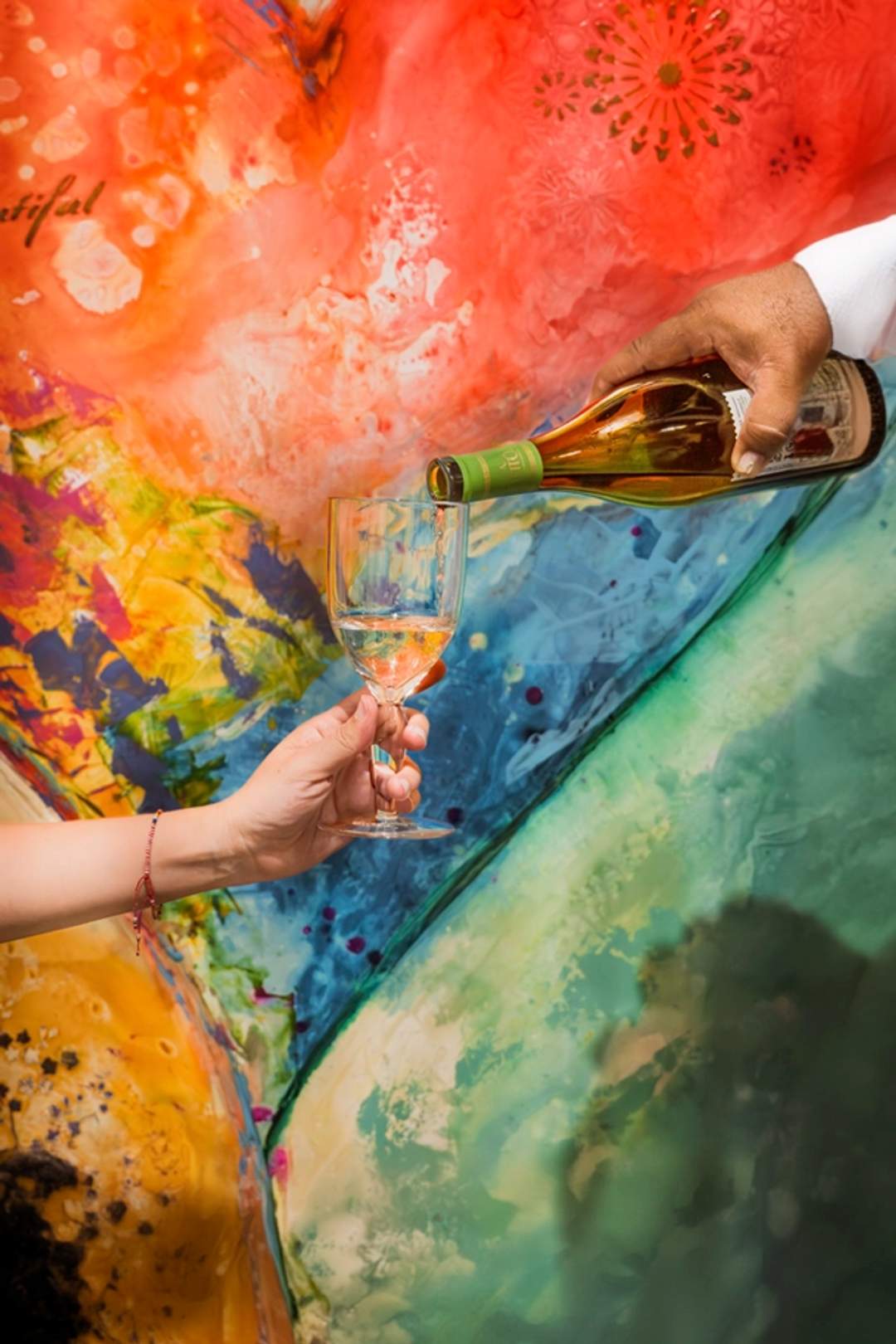 A close-up of a wine being poured into a glass against a colorful abstract background during an art and wine event.
