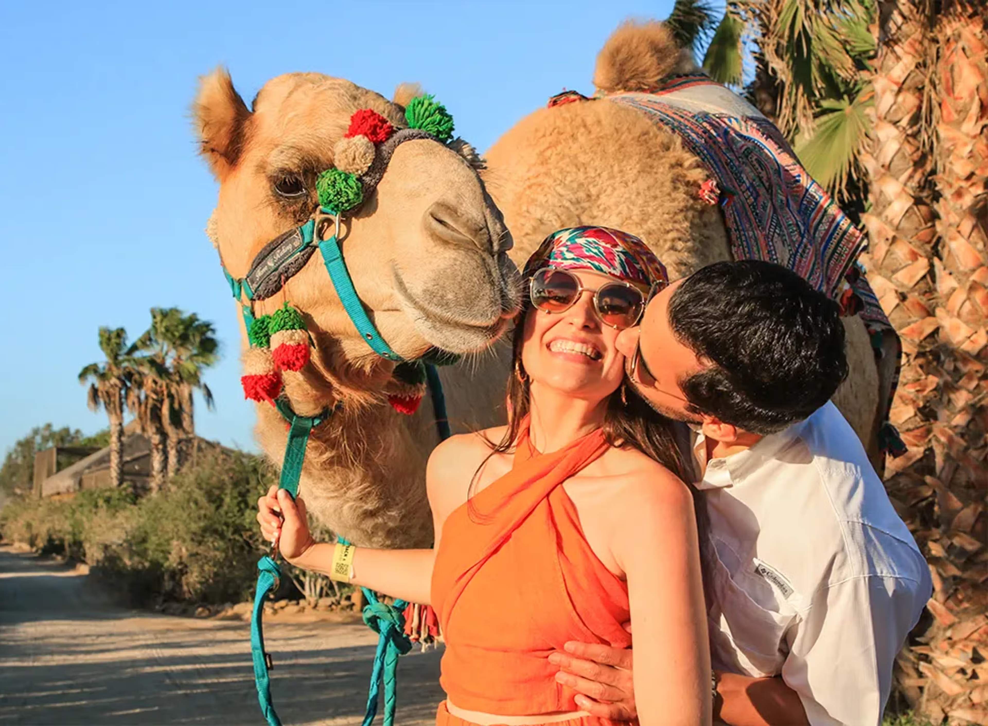 Couple beside a camel at Tierra Sagrada with Cabo Adventures as the man kisses the woman’s cheek.