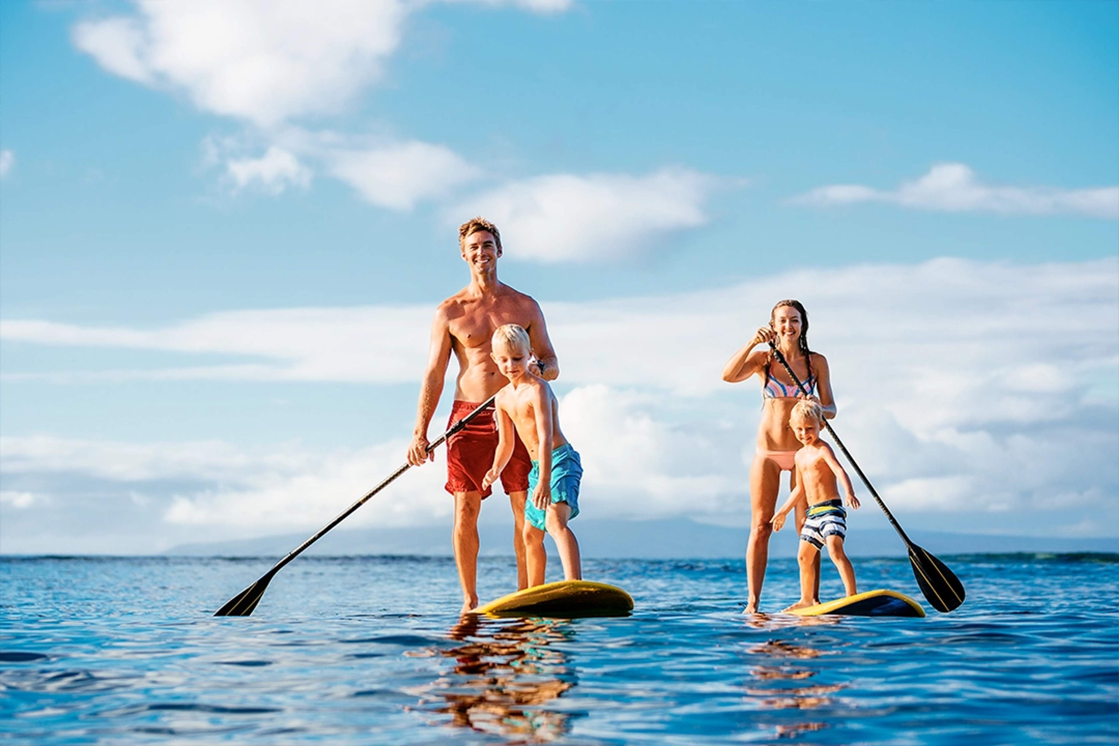 Family enjoying paddleboarding on calm waters under a clear sky, perfect for water activities.