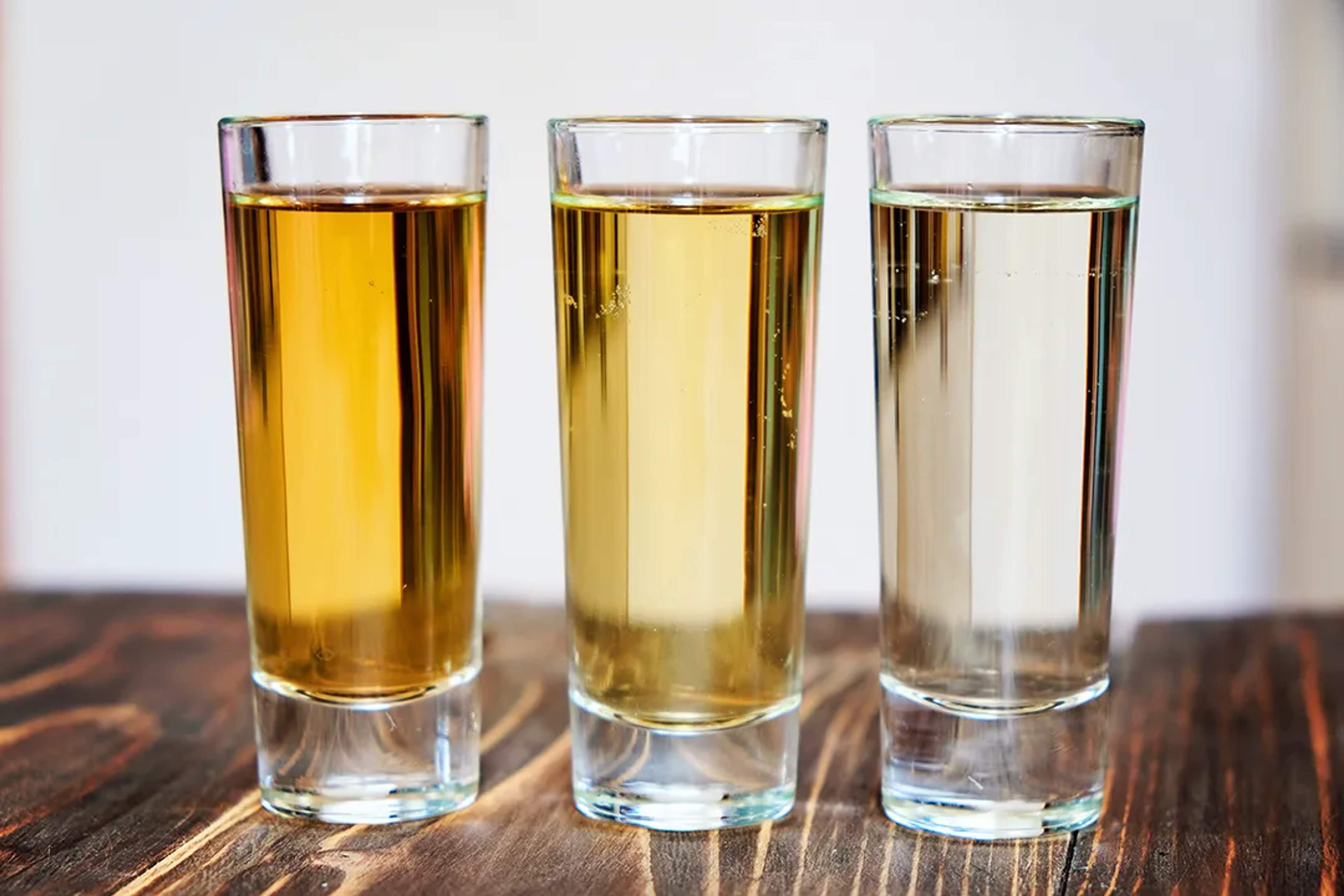Three tequila shots—añejo, reposado, and blanco—lined up on a wooden surface.