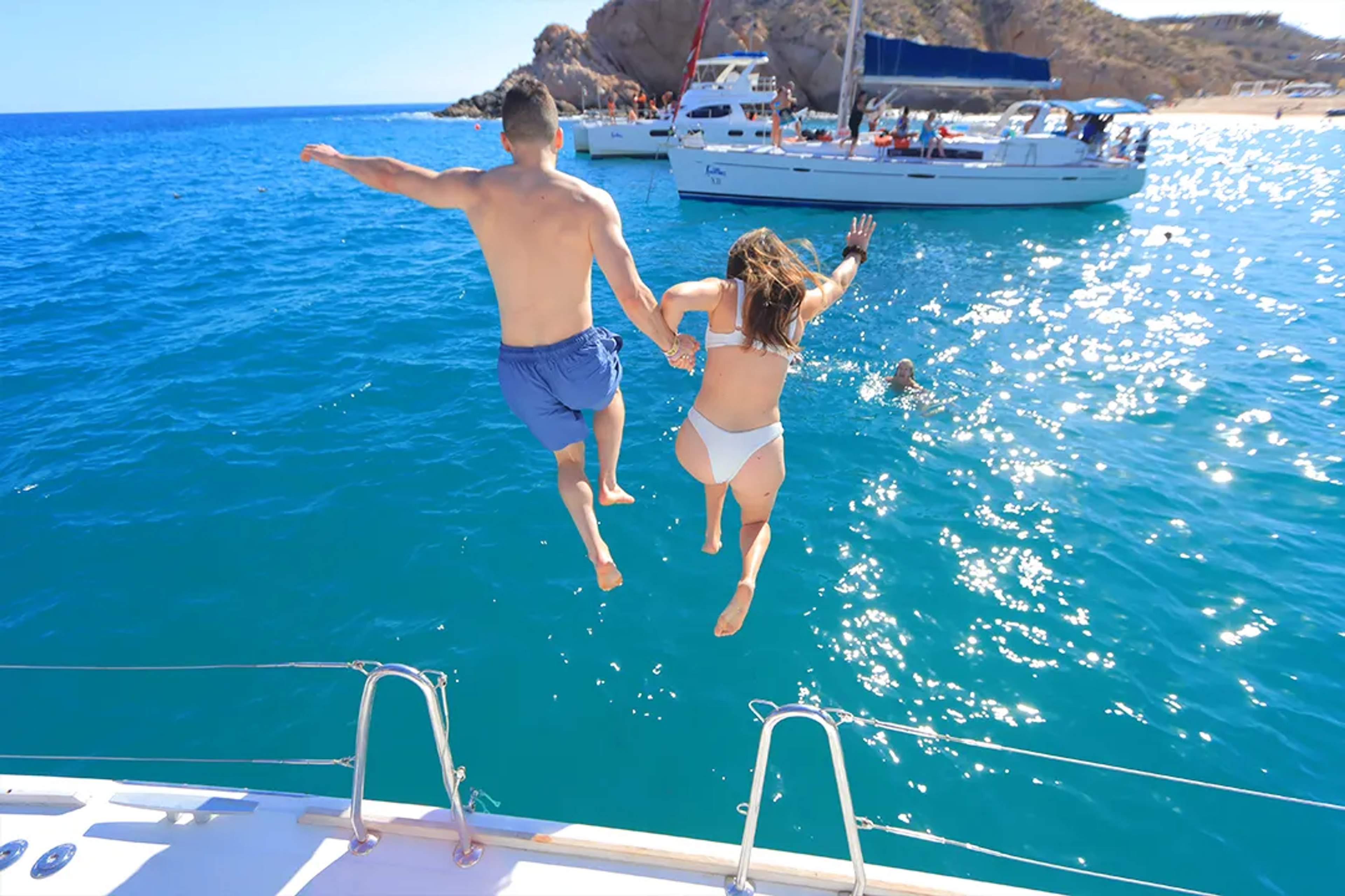 Couple jumping into turquoise waters from a catamaran in Los Cabos during a fun snorkeling and sailing tour