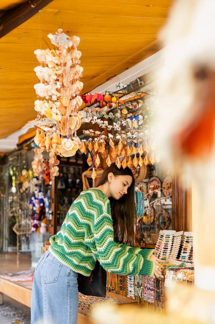 Una mujer explora un mercado vibrante en Cabo San Lucas, admirando joyería artesanal y decoraciones marinas.