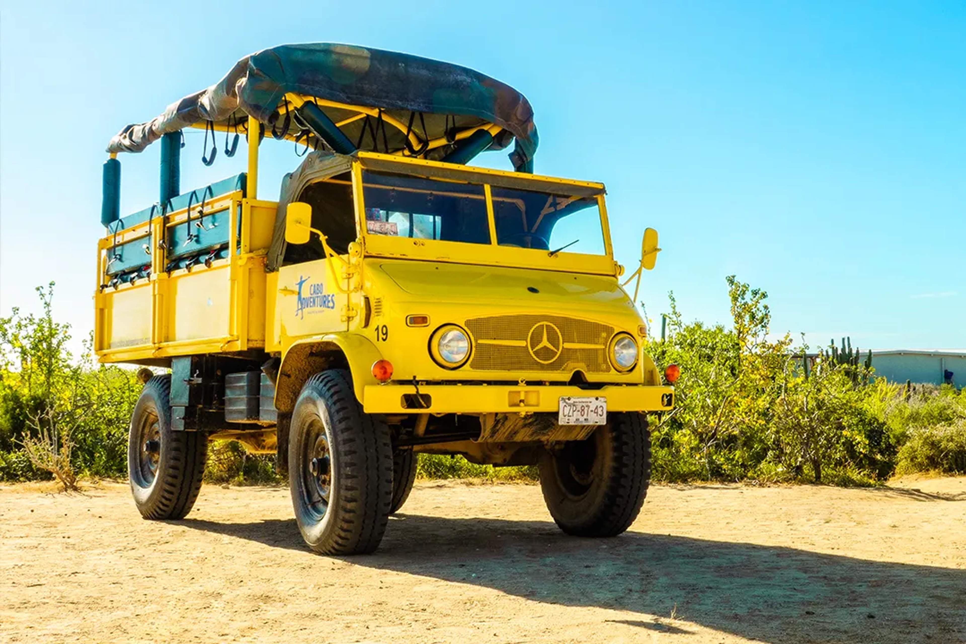 Unimog amarillo de Cabo Adventures listo para un tour por el desierto bajo un cielo despejado.