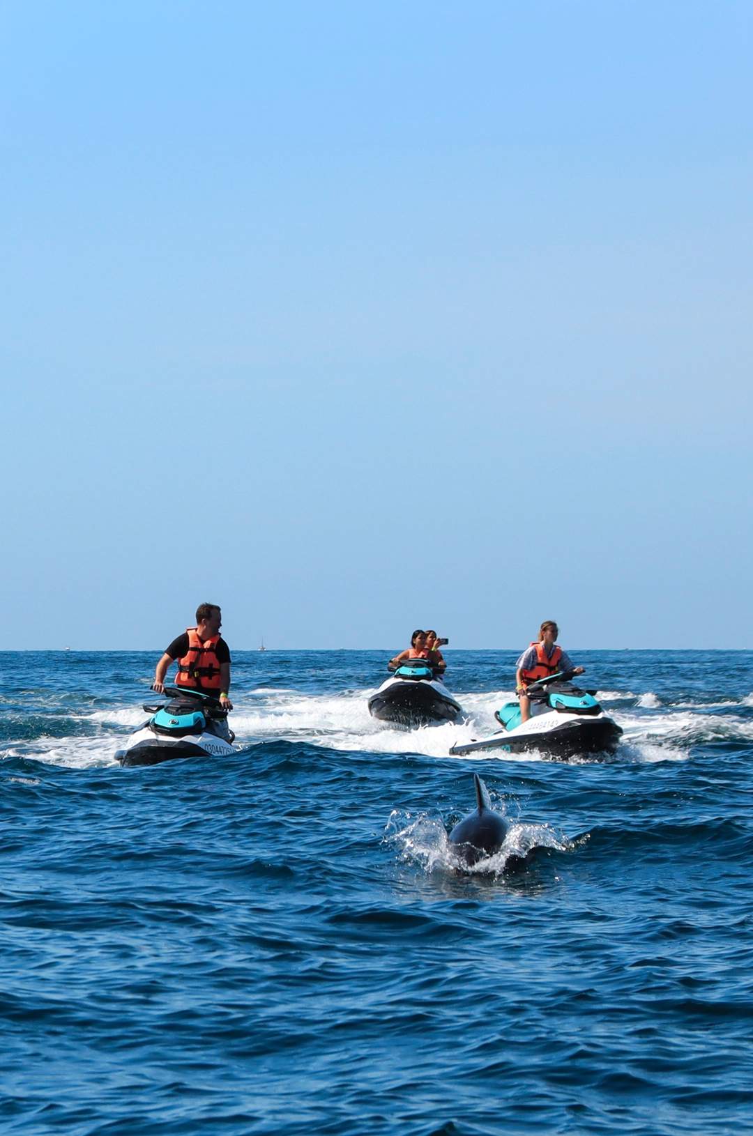A group of people riding jet skis in the ocean, with a dolphin jumping out of the water nearby.