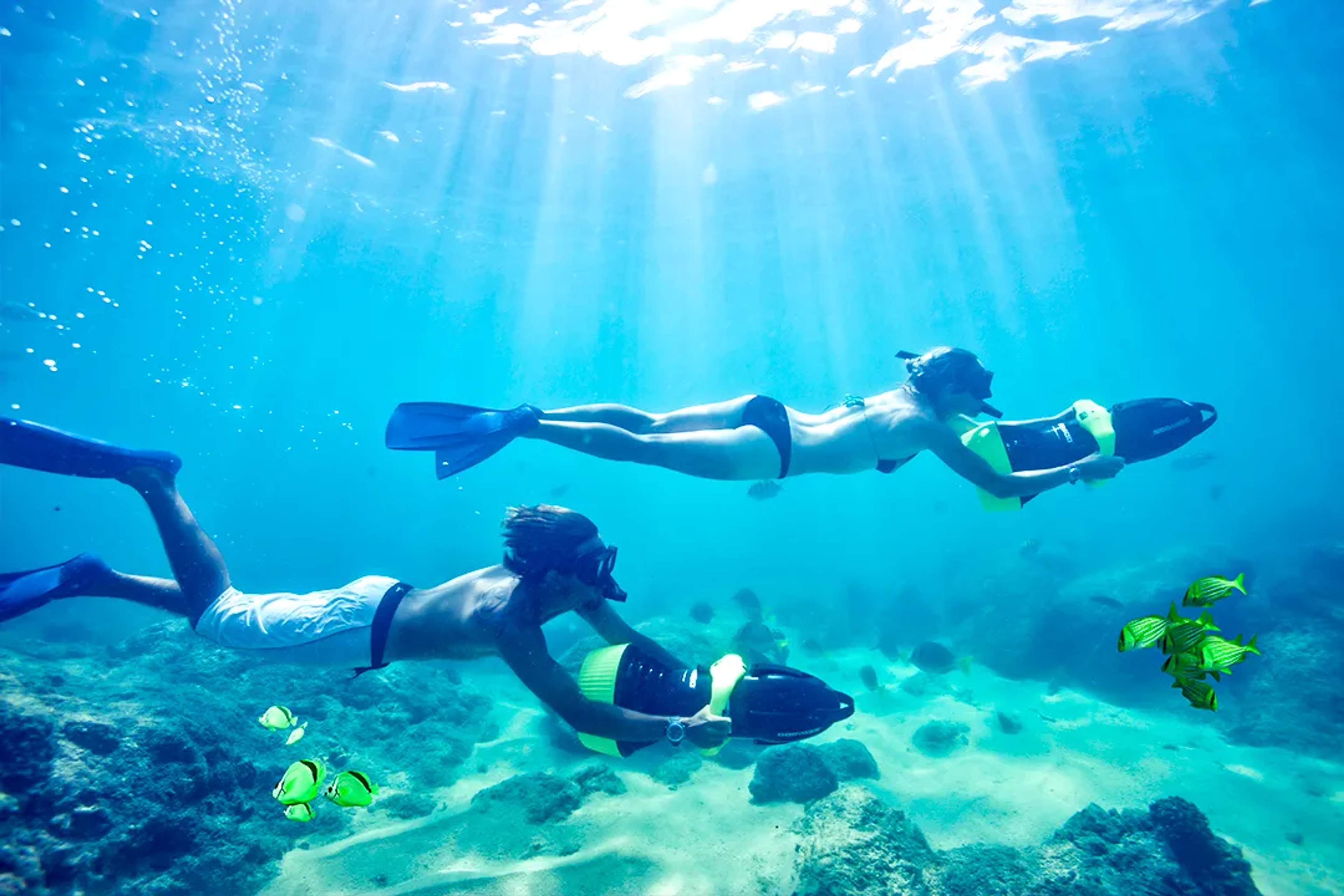 Couple snorkeling in crystal-clear tropical waters with sea scooters, coral reef and colorful fish below