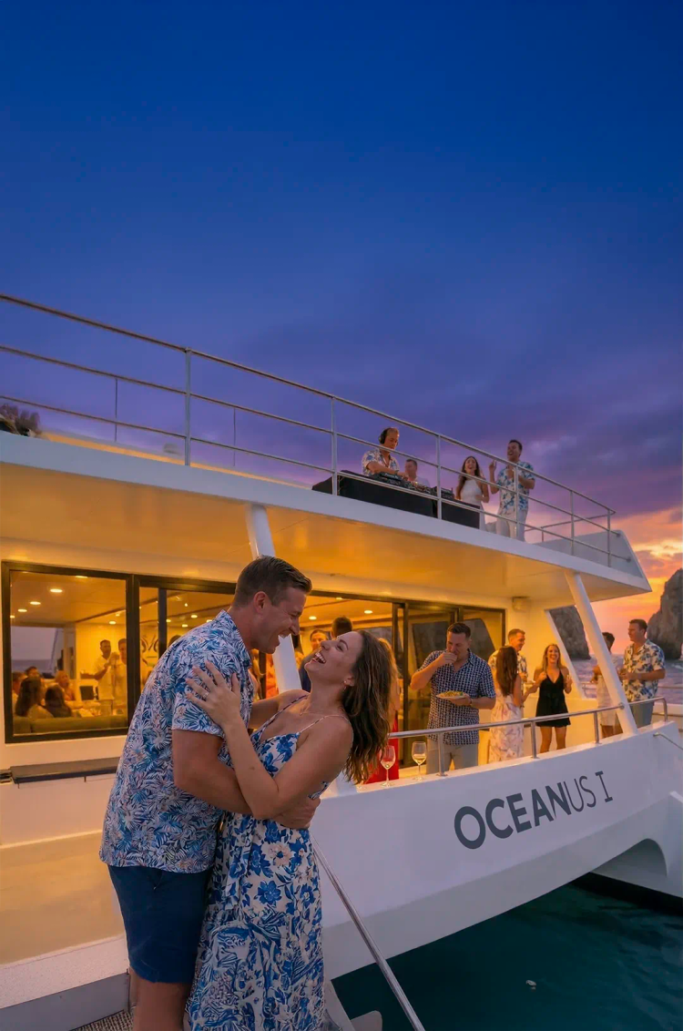Pareja bailando en crucero Oceanus al atardecer en Cabo con música, bebidas y vistas al Arco