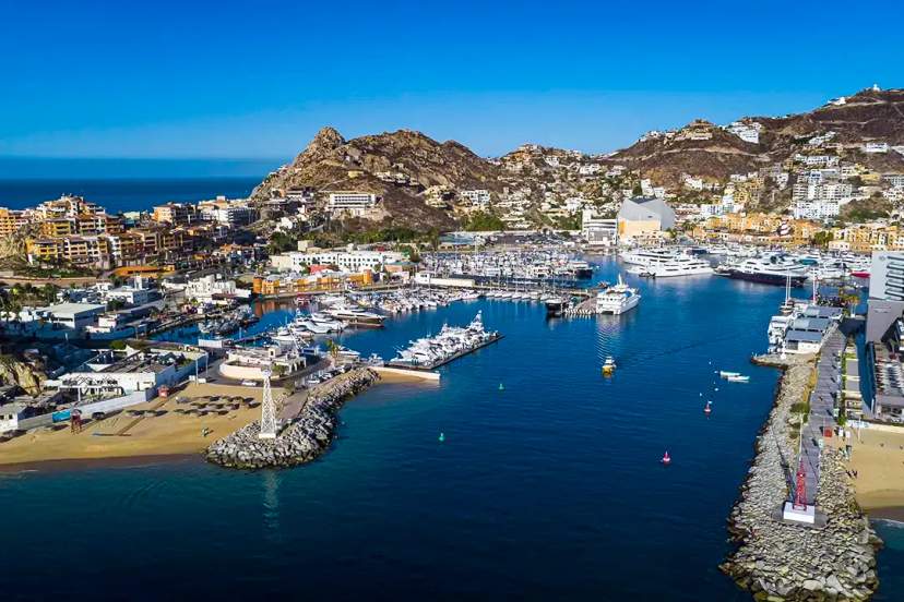 Aerial view of Cabo San Lucas Marina, with yachts, beaches, and hills under a clear blue sky.