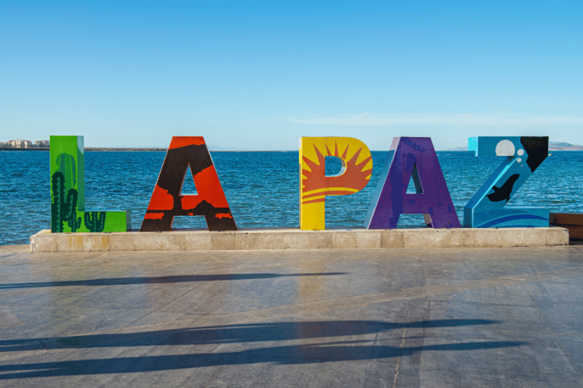 Colorful "LA PAZ" sign by the waterfront, with the sea and sky in the background.