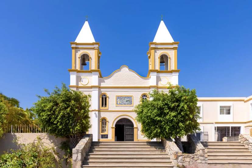 Fachada colonial blanca y dorada con dos campanarios bajo un cielo azul despejado en San José del Cabo
