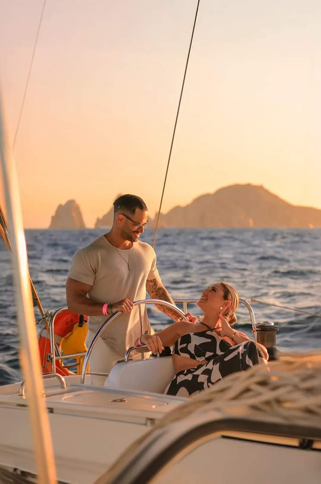 Couple enjoying a sunset sail in Cabo, smiling and relaxing with scenic ocean views and mountains in the background.