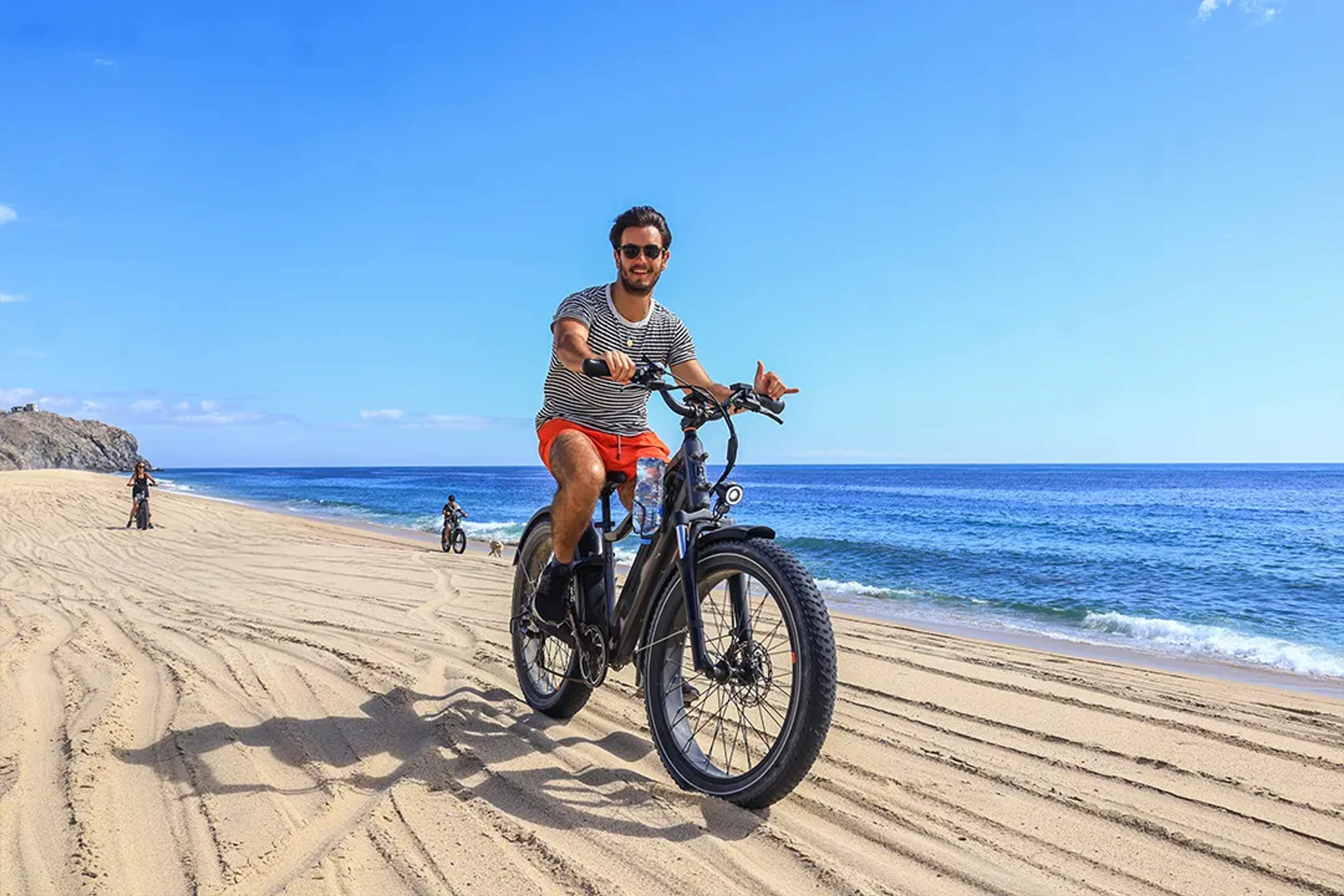 Man riding electric bike on sandy beach along ocean coastline in Los Cabos under clear blue sky