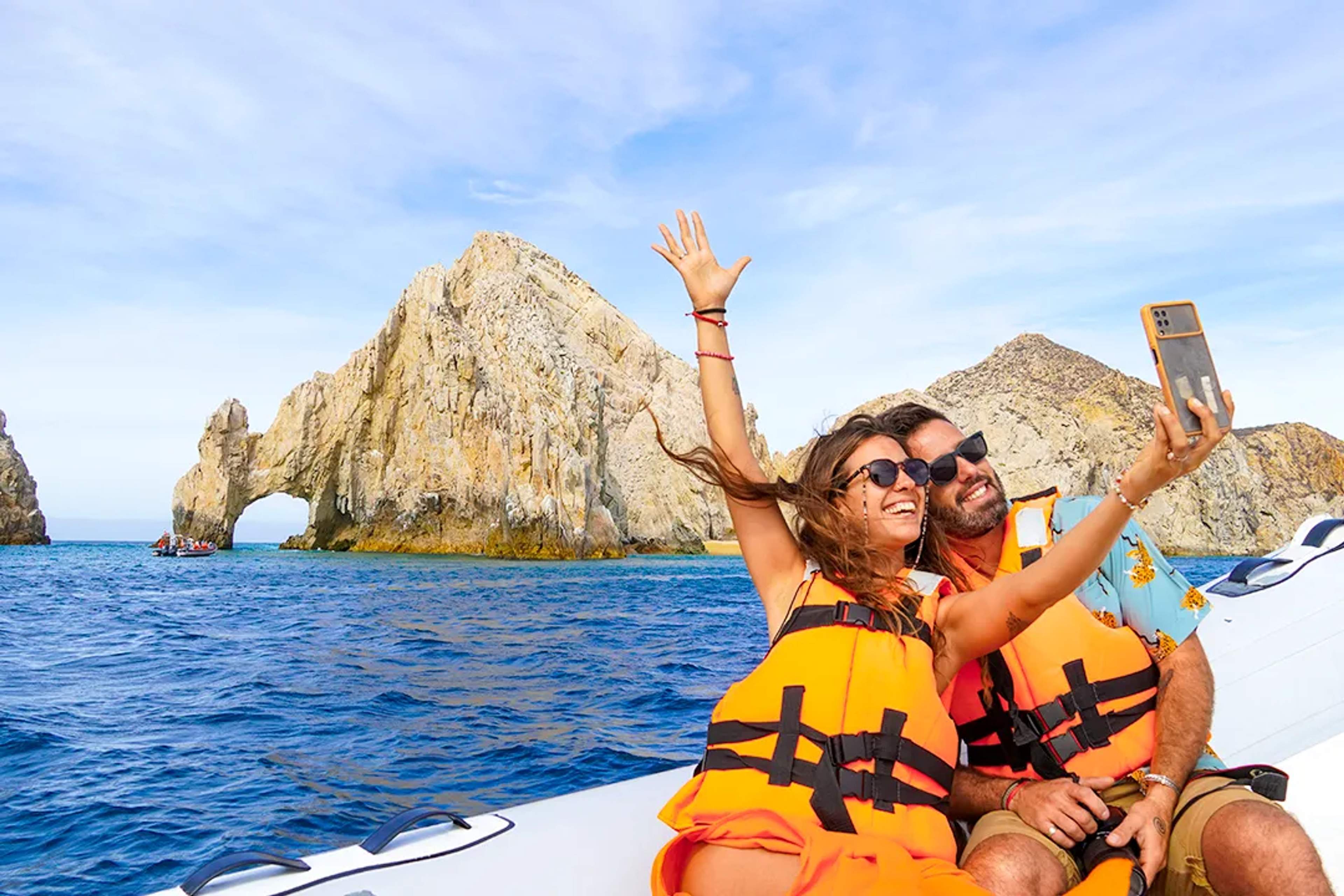 Couple enjoying a boat tour in Cabo San Lucas taking photos near the iconic Arch and dramatic rock formations