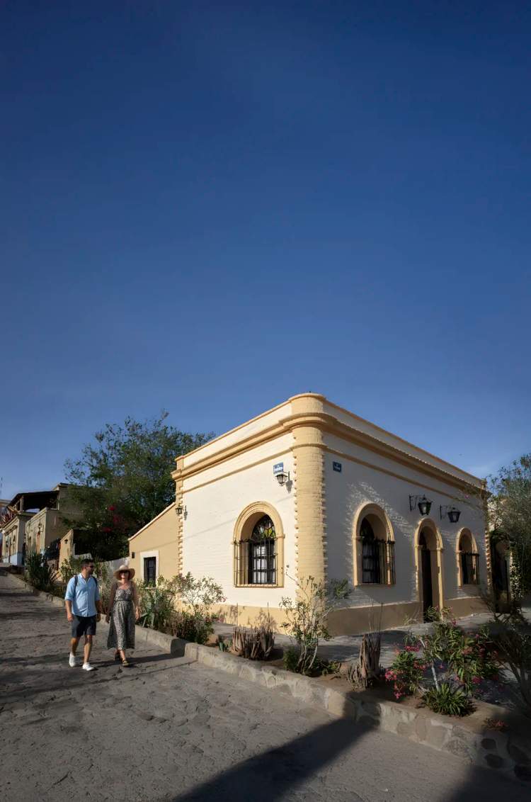 Visitantes recorren calles empedradas de El Triunfo, Baja California Sur, admirando edificios históricos restaurados.