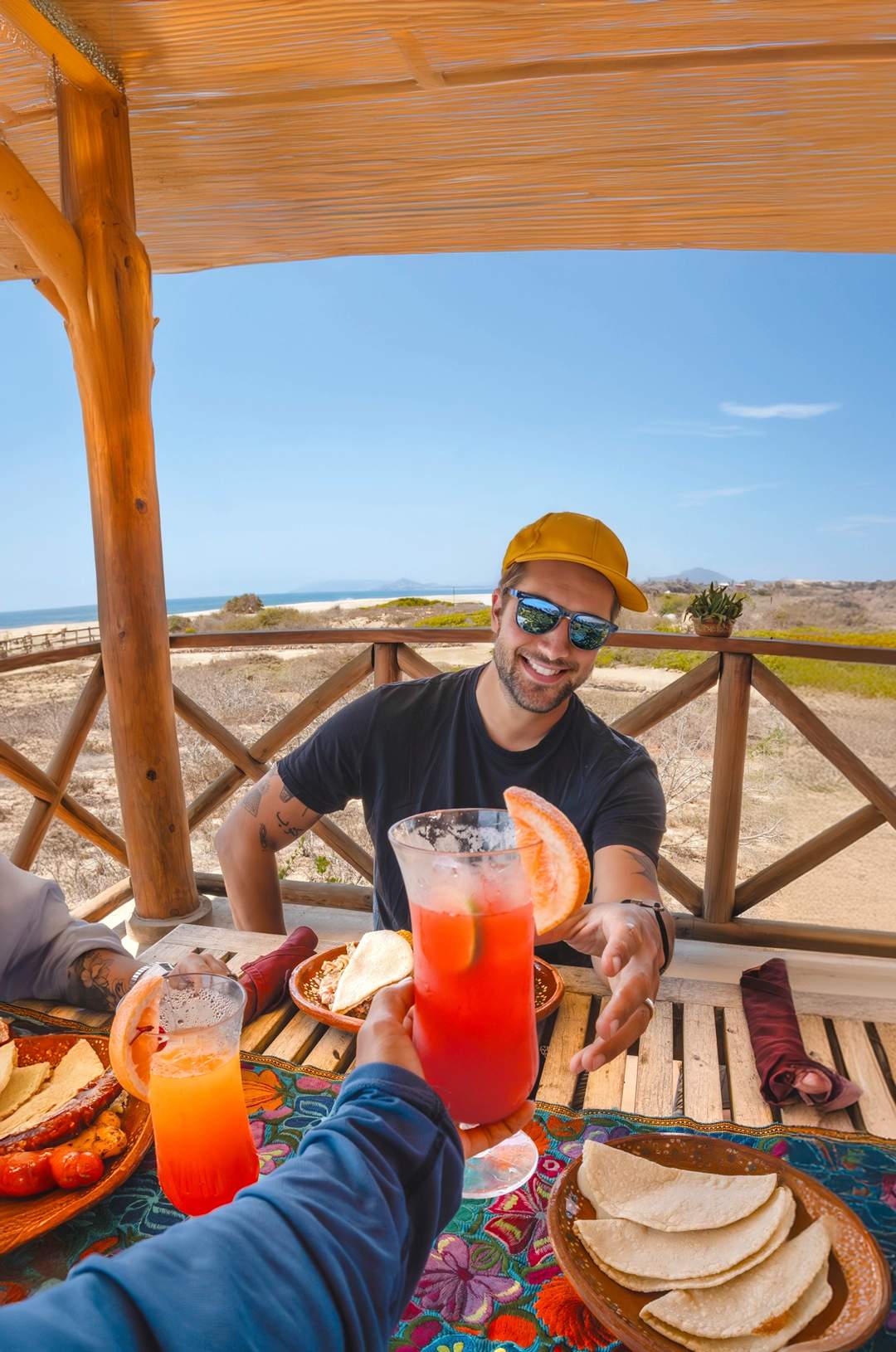 Group of friends toasting with cocktails at an outdoor table by the sea, enjoying the scenery.