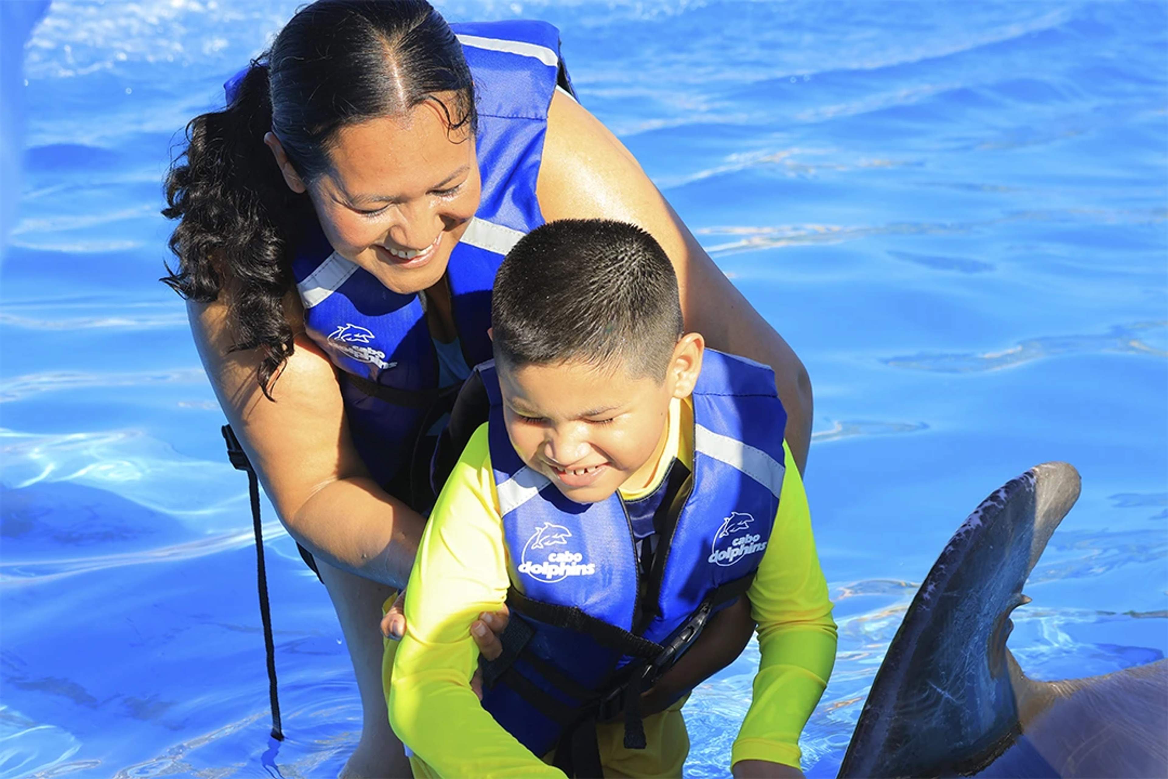 A woman and a child enjoy a dolphin experience at Cabo Dolphins, both wearing life jackets.
