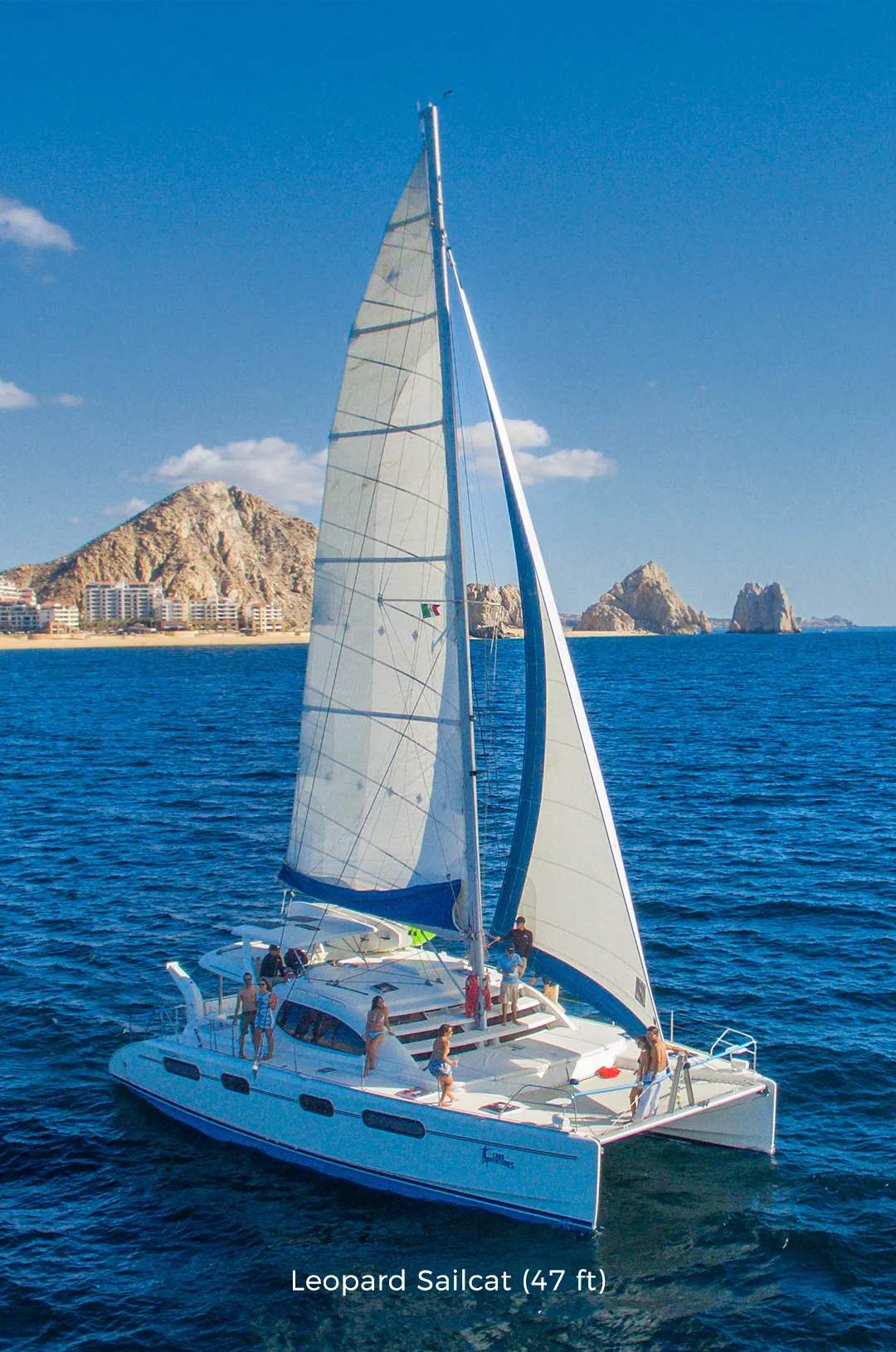Sailboat cruising near Cabo San Lucas with scenic coastline and iconic rock formations in the background.