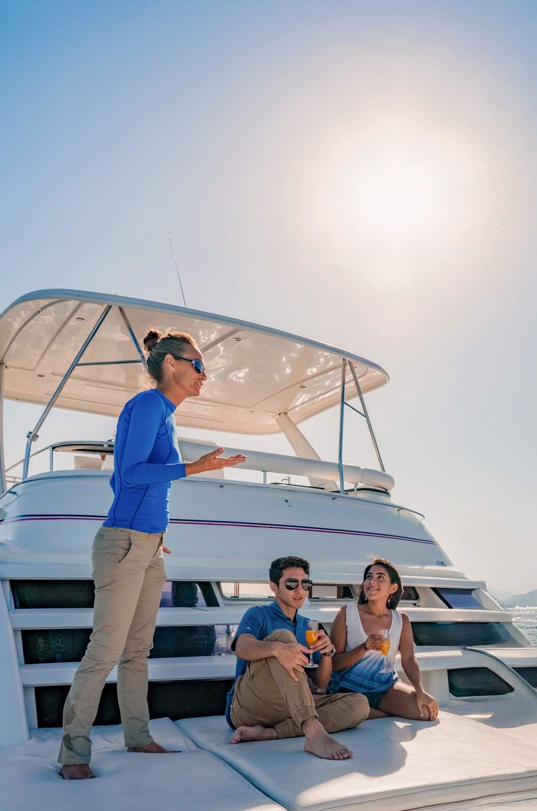 Group of friends relaxing with drinks on a luxury yacht, enjoying views of Cabo’s iconic rock formations under a sunny sky.