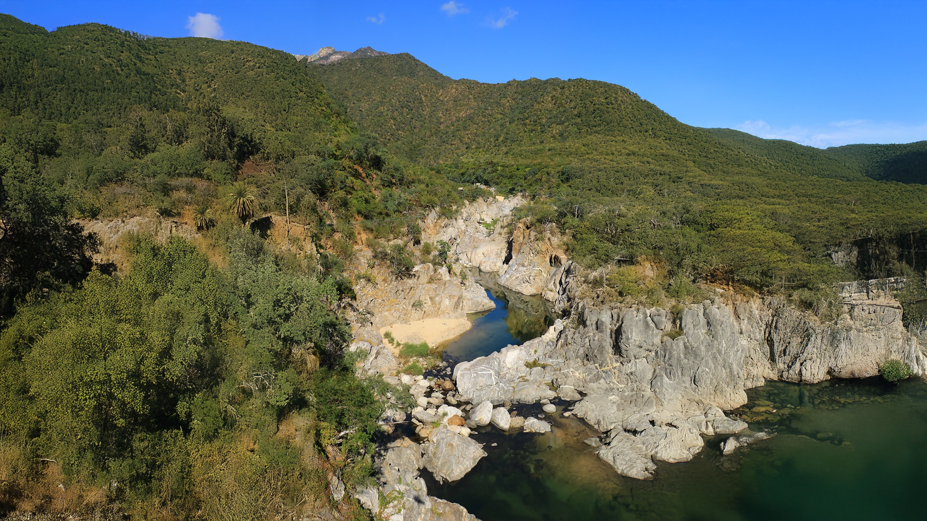 A scenic canyon with a river flowing through rocky terrain, surrounded by lush green forests and hills.