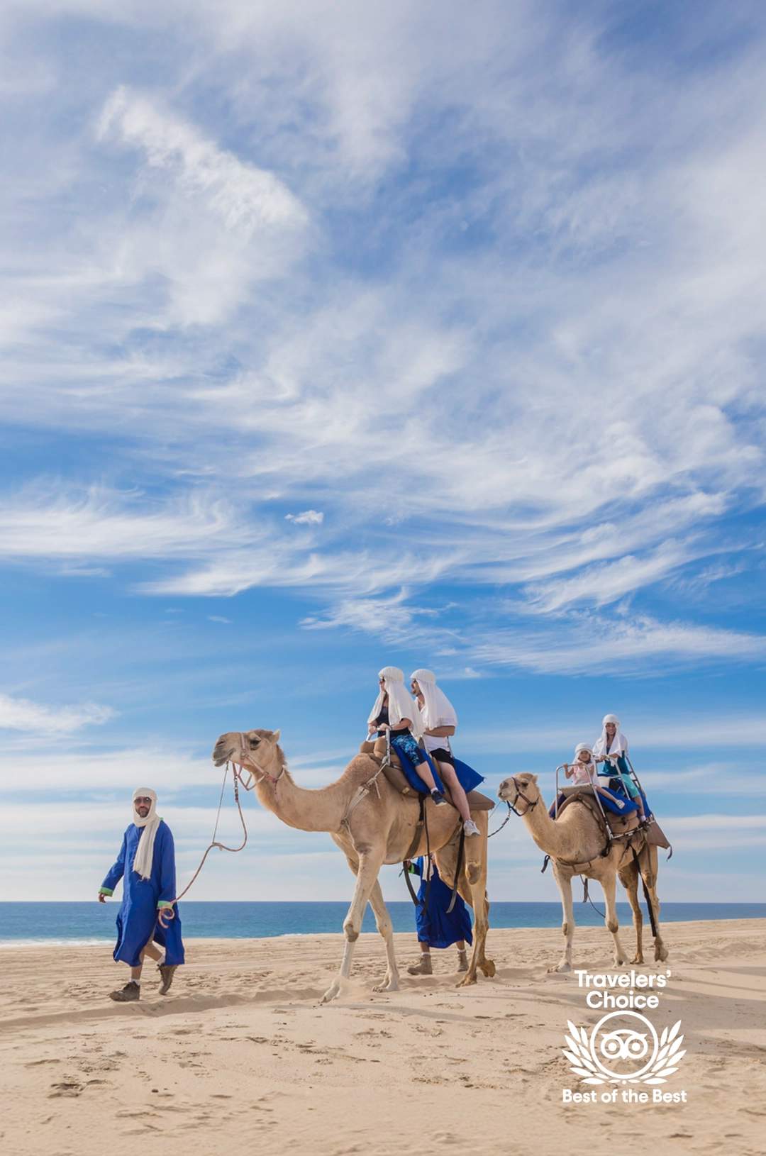 Group of people riding camels on a desert beach, led by a local guide