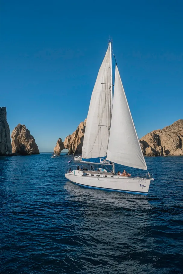 White sailboat glides on calm blue ocean under a clear sky, with passengers enjoying the serene day.