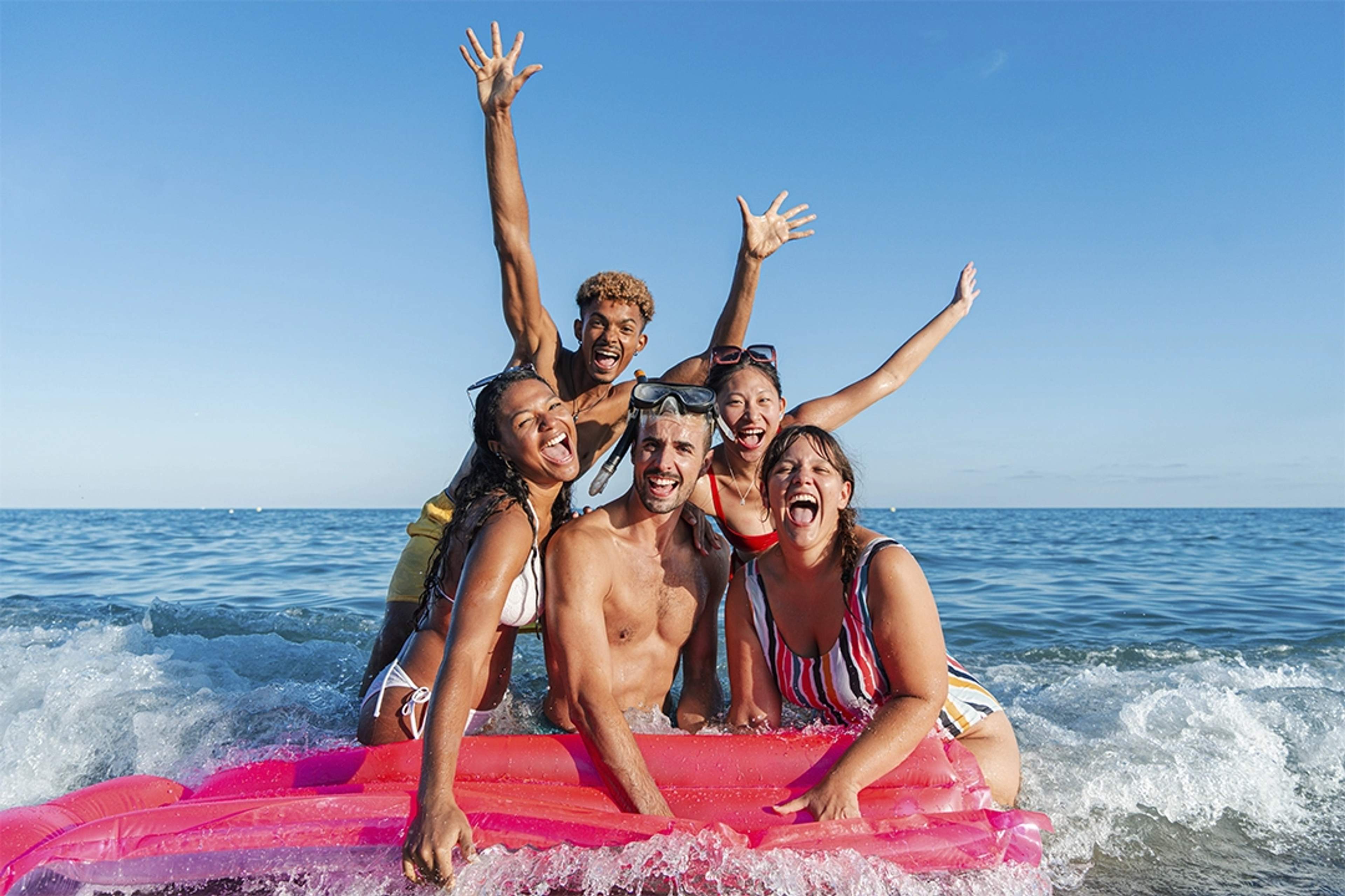 Group of friends enjoying the water with an inflatable mat, laughing and celebrating.