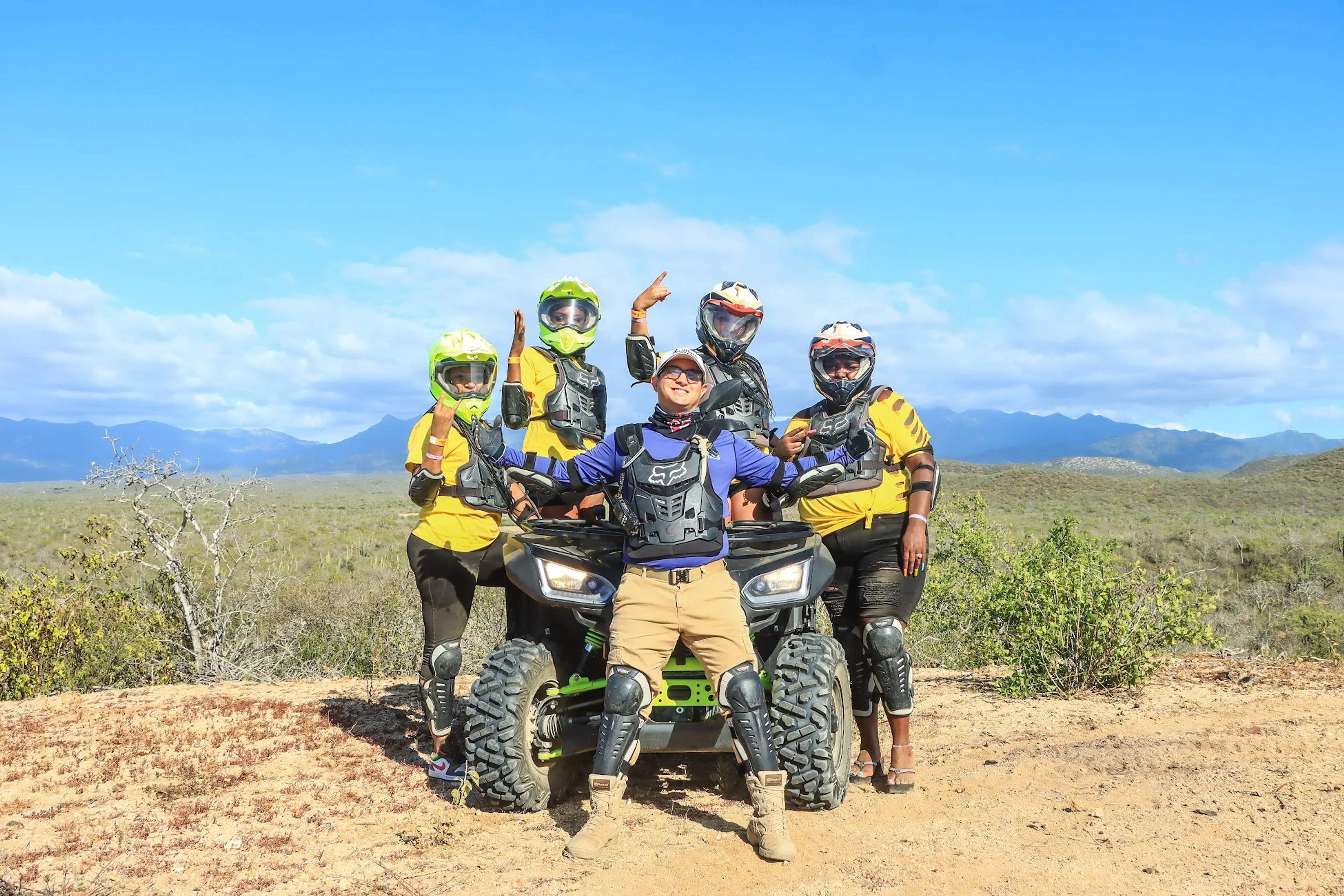 group of five people posing with an ATV in a natural setting, during an adventure tour