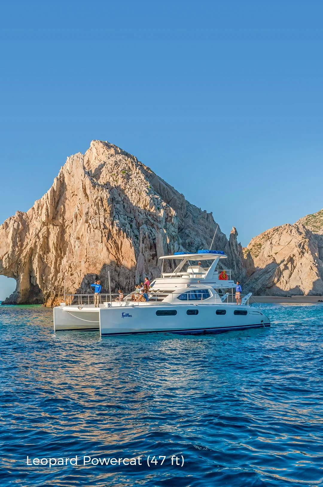 Yacht anchored near Cabo’s iconic rock arch under a clear blue sky, with people enjoying the scenic view.