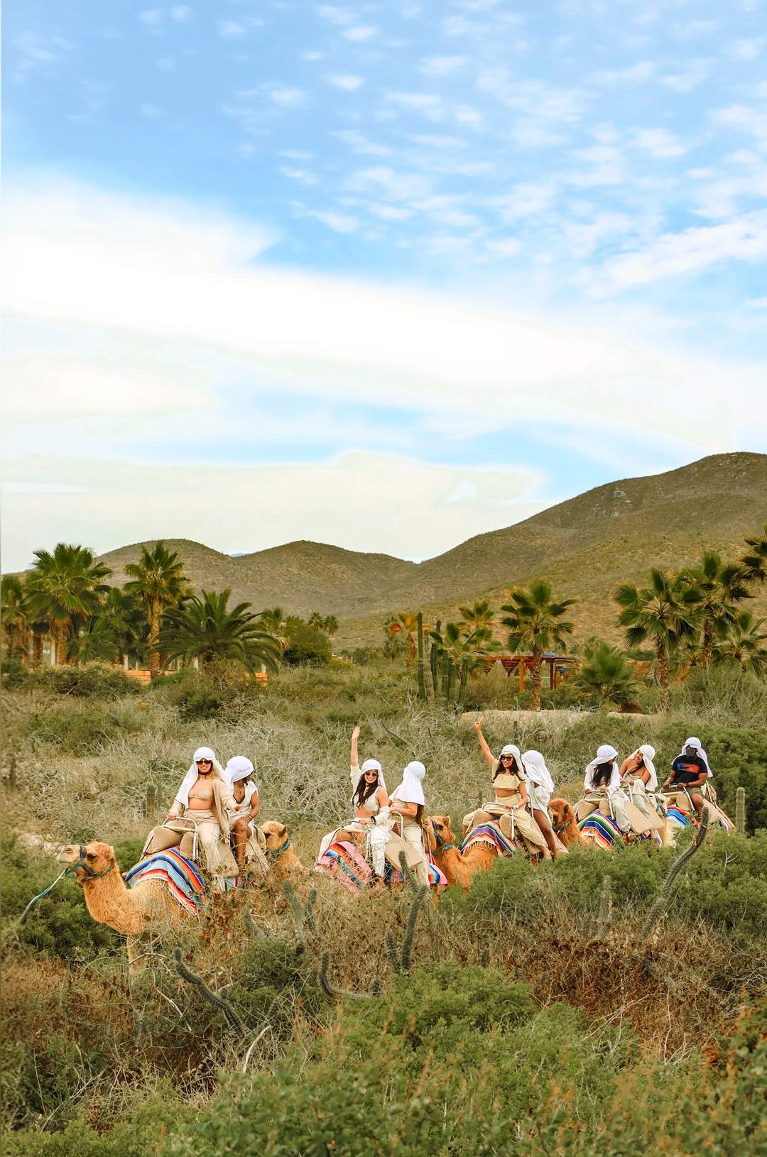 Group of people riding camels in a line, guided by a guide, in a desert landscape