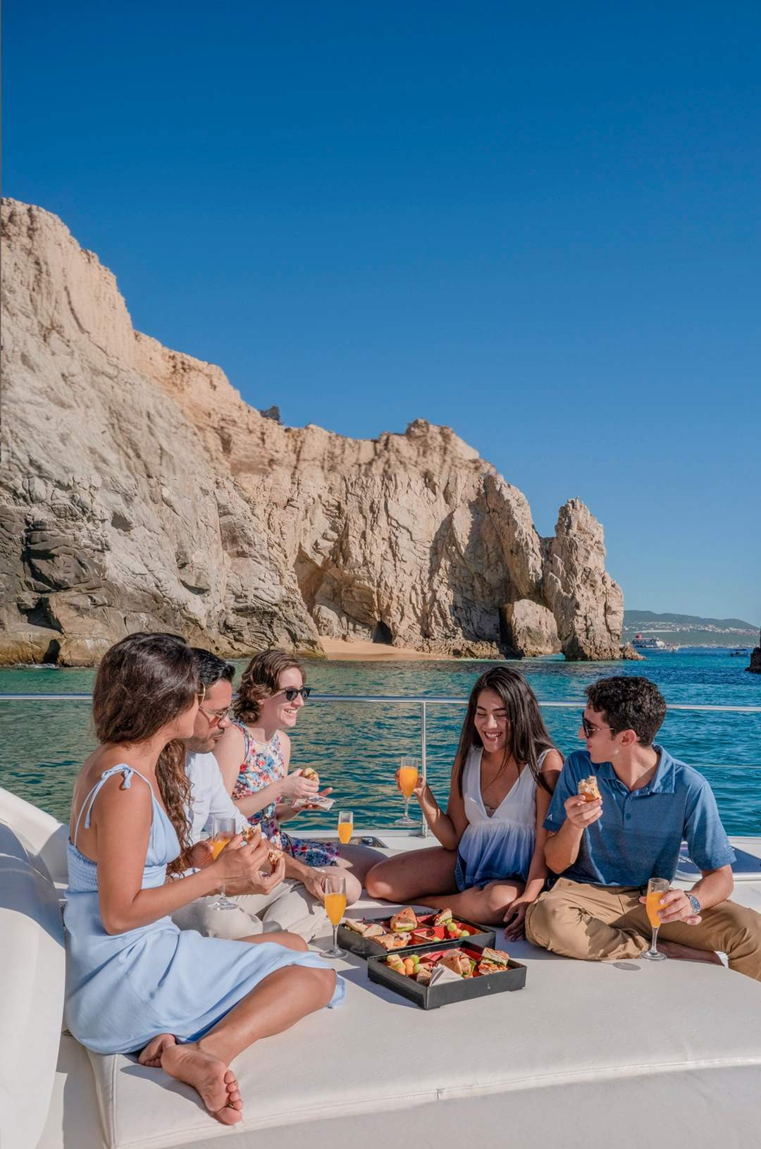 A group of friends enjoying a meal and drinks on a luxury yacht near rocky cliffs in Cabo.