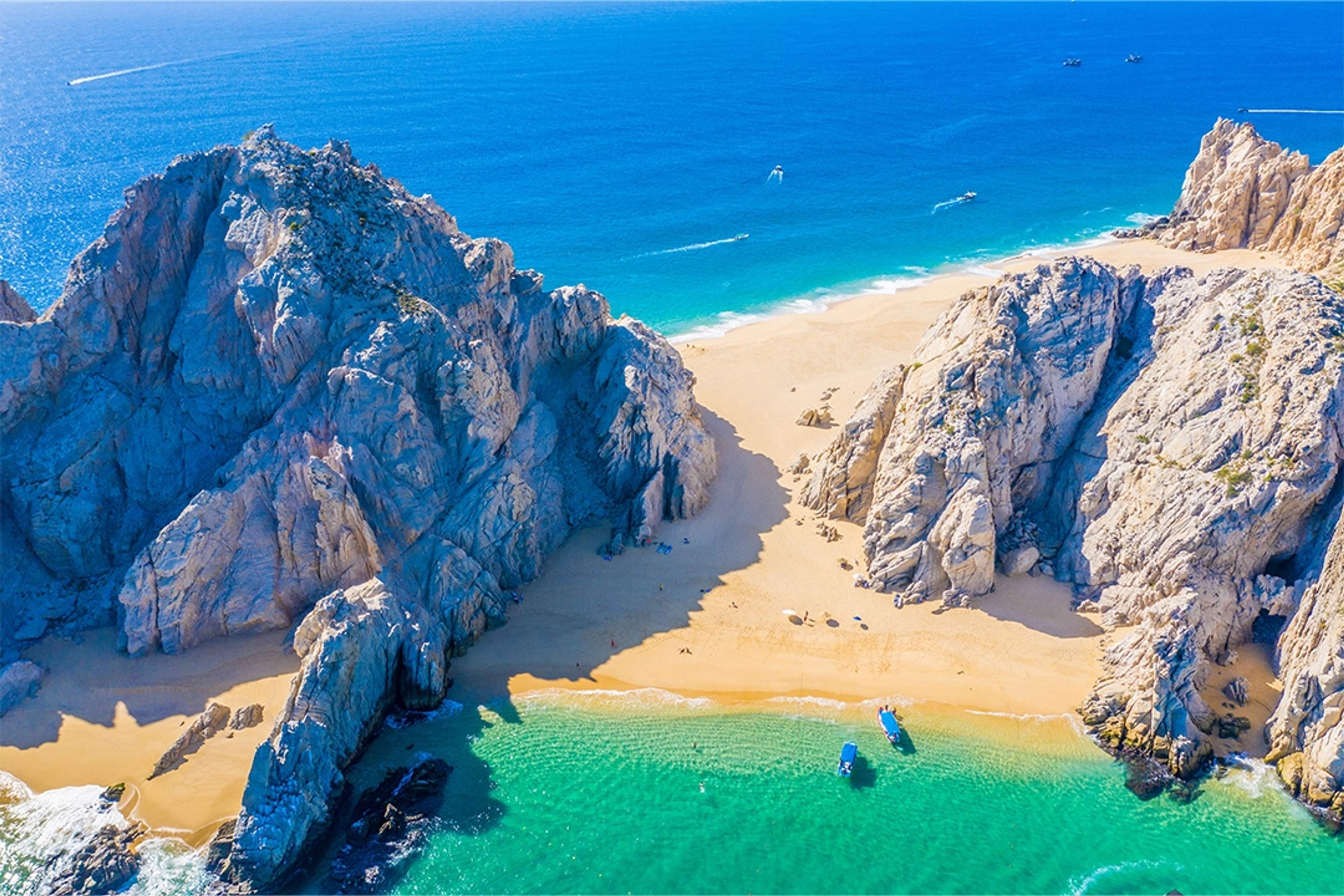 Hidden beach nestled between rock formations in Cabo San Lucas, with crystal-clear waters and golden sand.