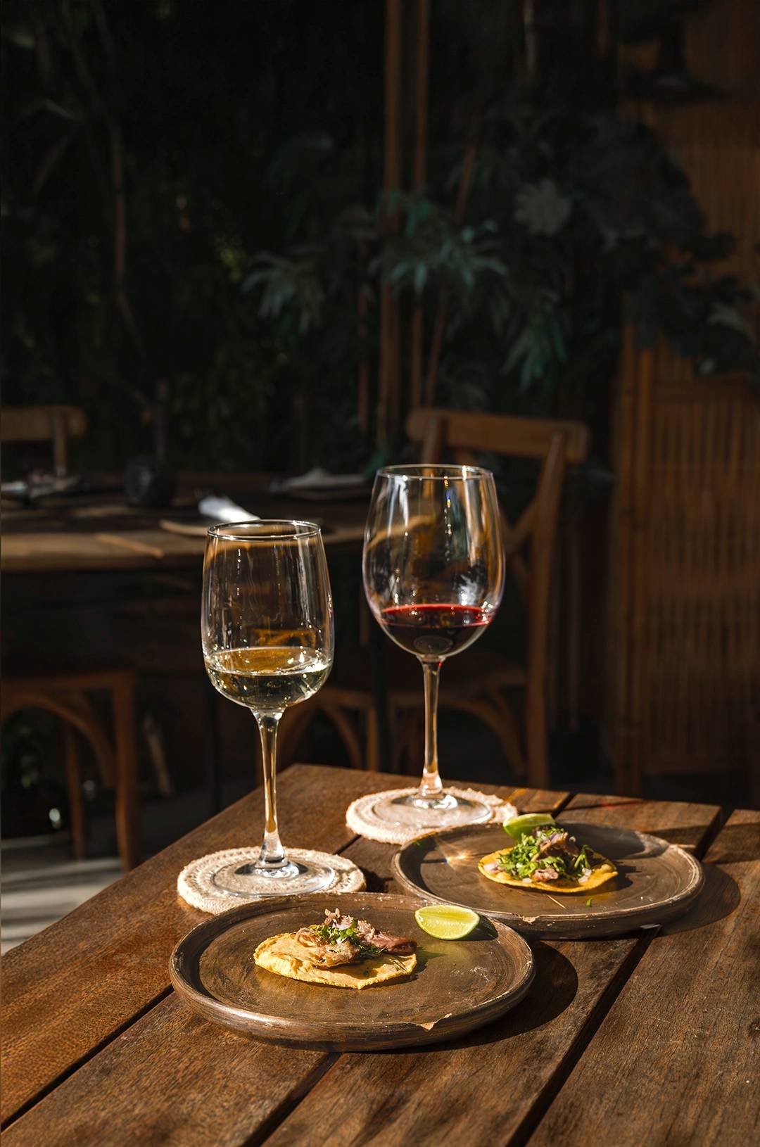 Two glasses of wine with plated appetizers on a rustic wooden table, set in a cozy outdoor ambiance.