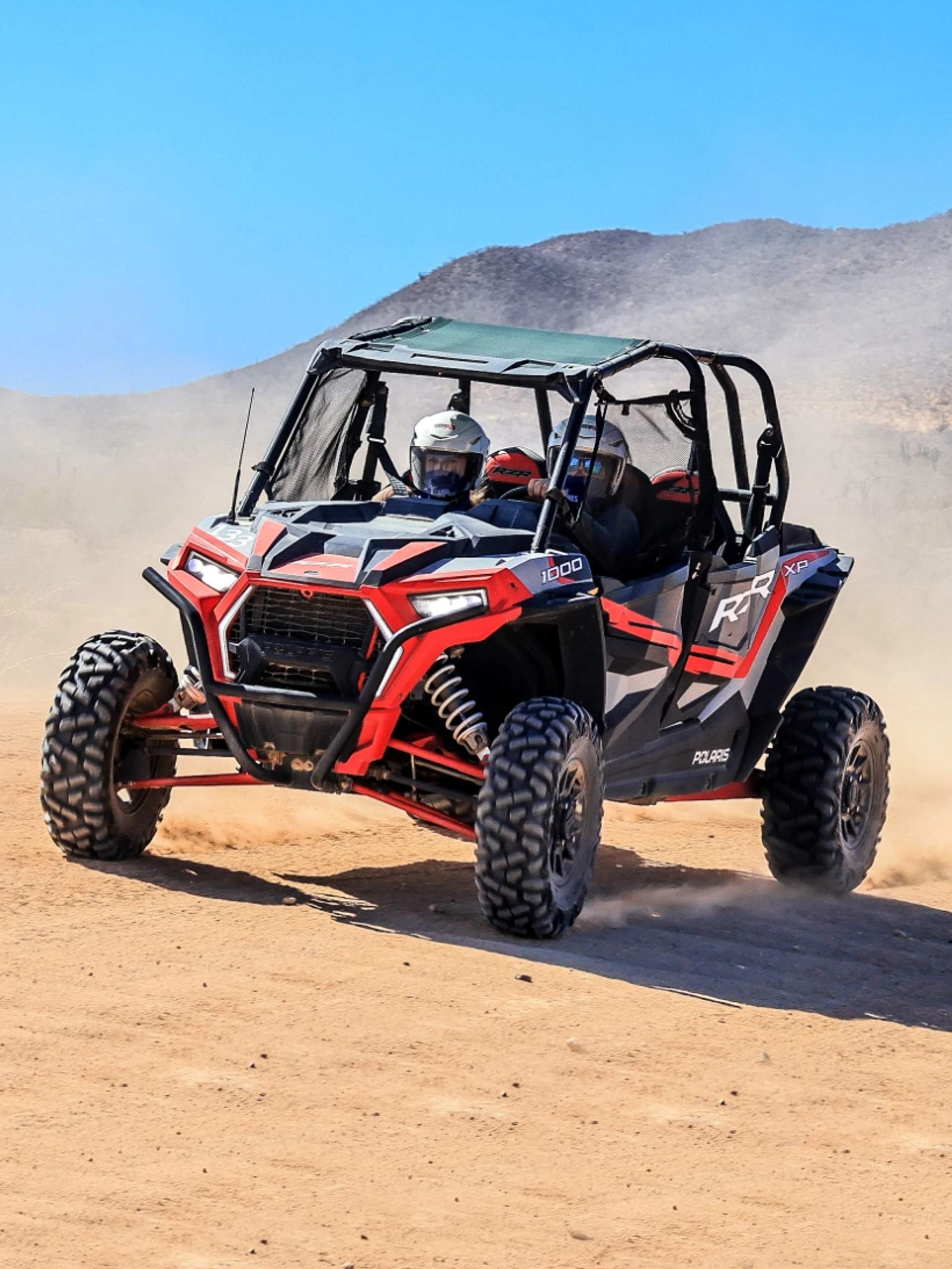 An ATV powers through the desert with two riders wearing helmets, capturing the thrill of the ride.