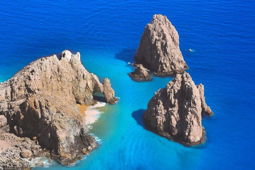 Rock Formations In Turquoise Ocean Waters, With A Small Sandy Beach Between Them, Under A Bright Blue Sky