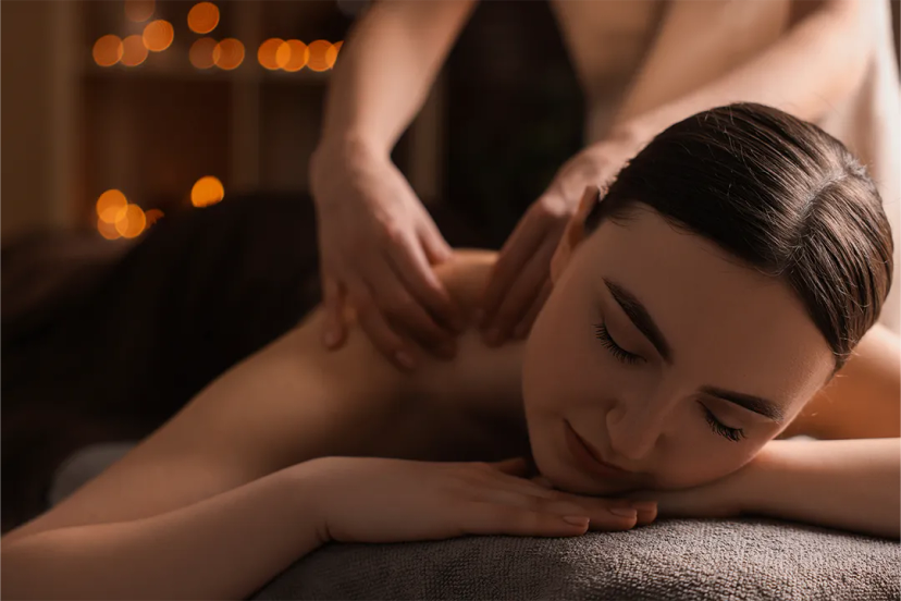 A woman enjoys a relaxing massage on her back in a dimly lit room with soft, warm lighting and blurred background lights.
