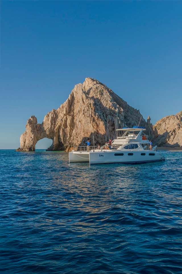 Luxury catamaran near Cabo’s iconic Arch, cruising over calm waters with clear skies.